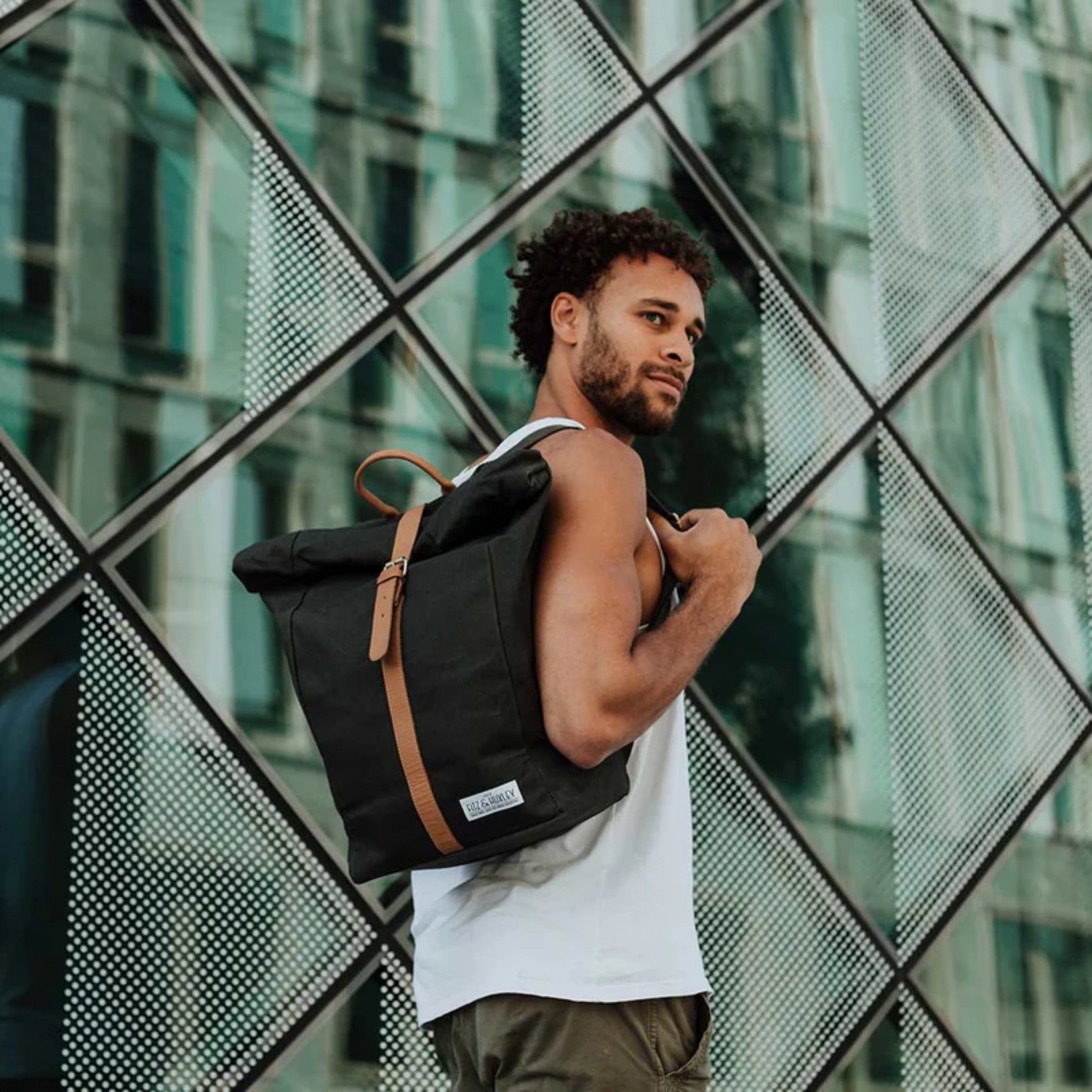 Mann mit schwarzem Rucksack steht vor einem modernen, gläsernen Gebäude mit rautenförmigen Strukturen.