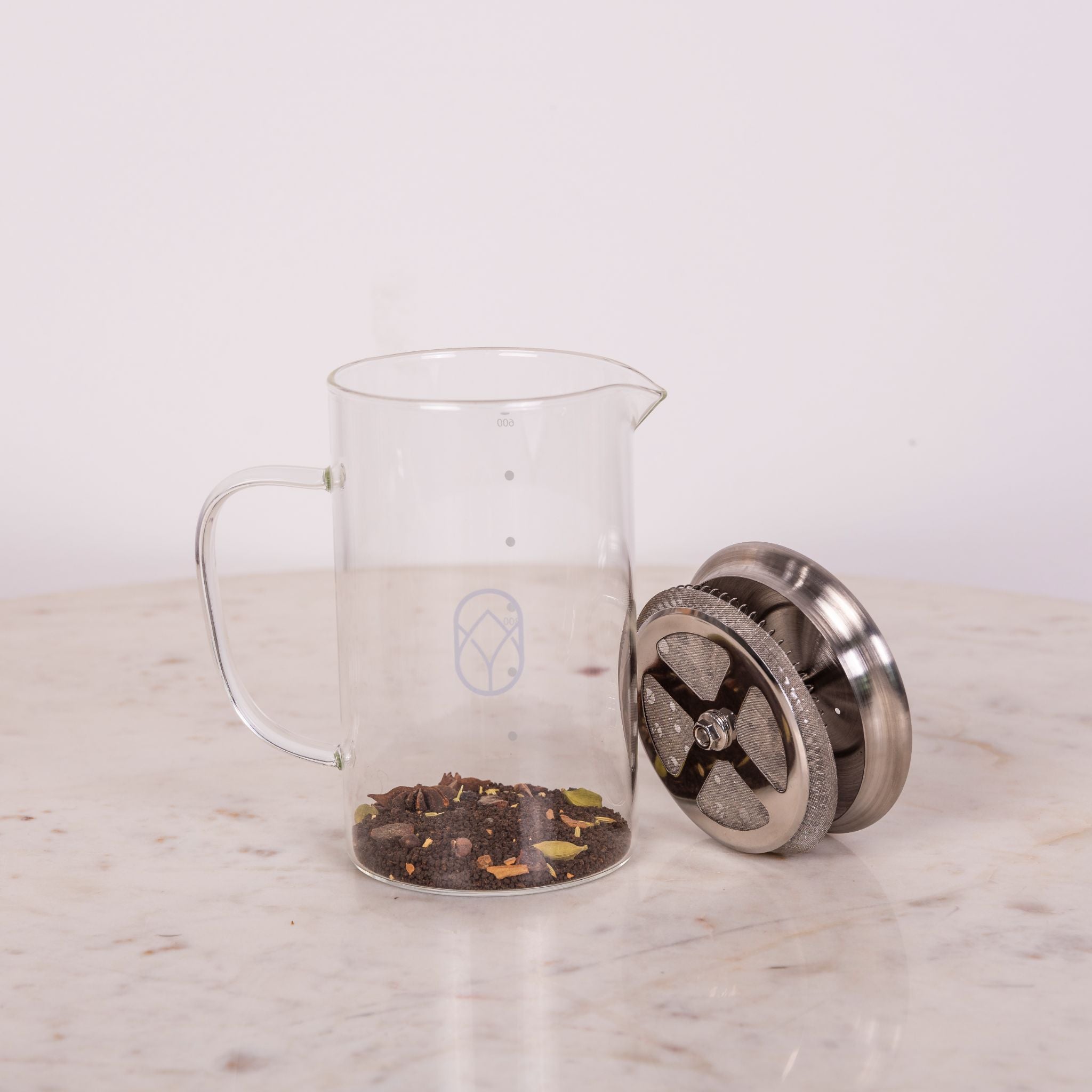 Glasbehälter mit losem Tee und ein Metallfilter liegen auf einem Marmortisch.