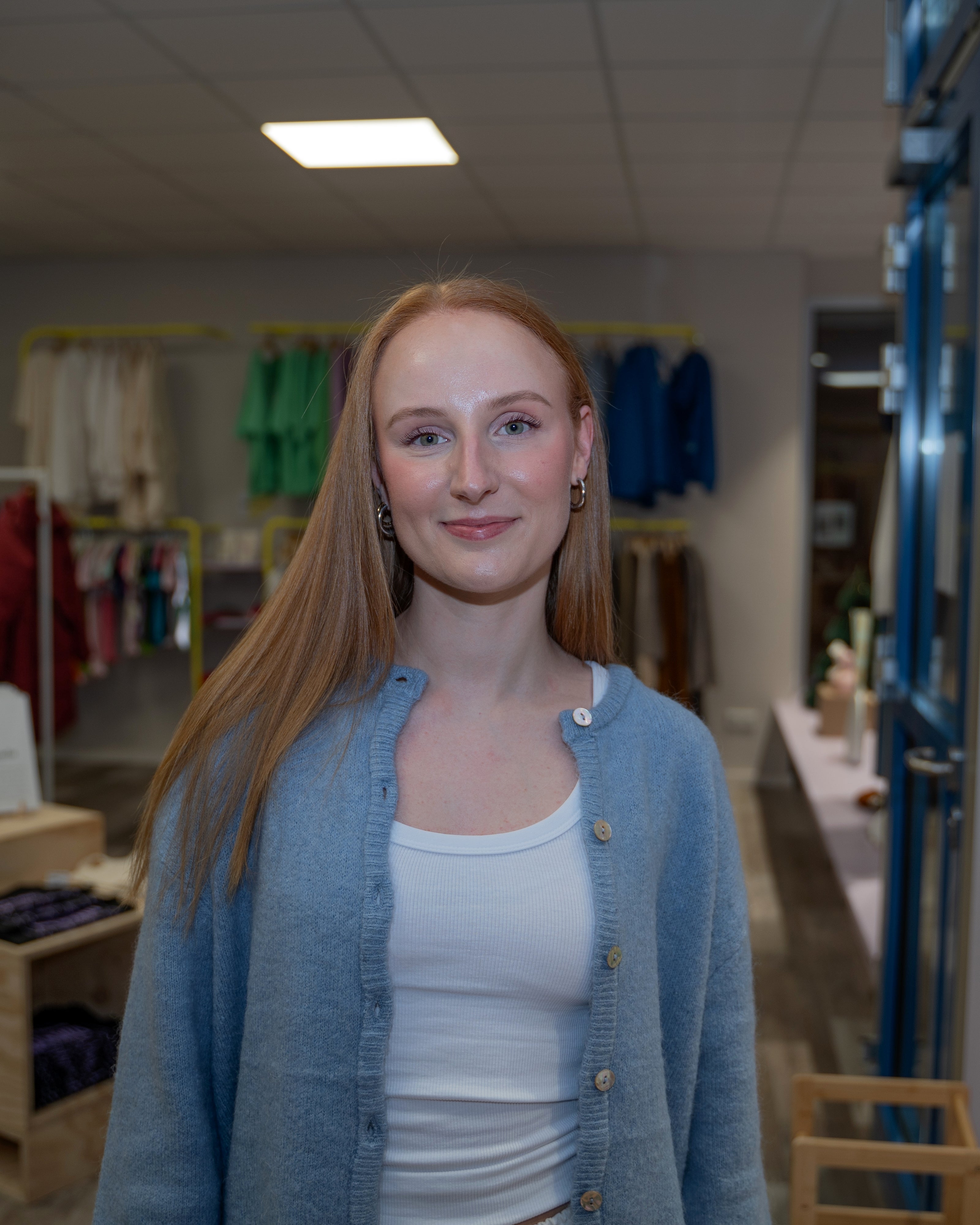 Eine Frau mit blauer Strickjacke lächelt in einem Bekleidungsgeschäft in die Kamera.