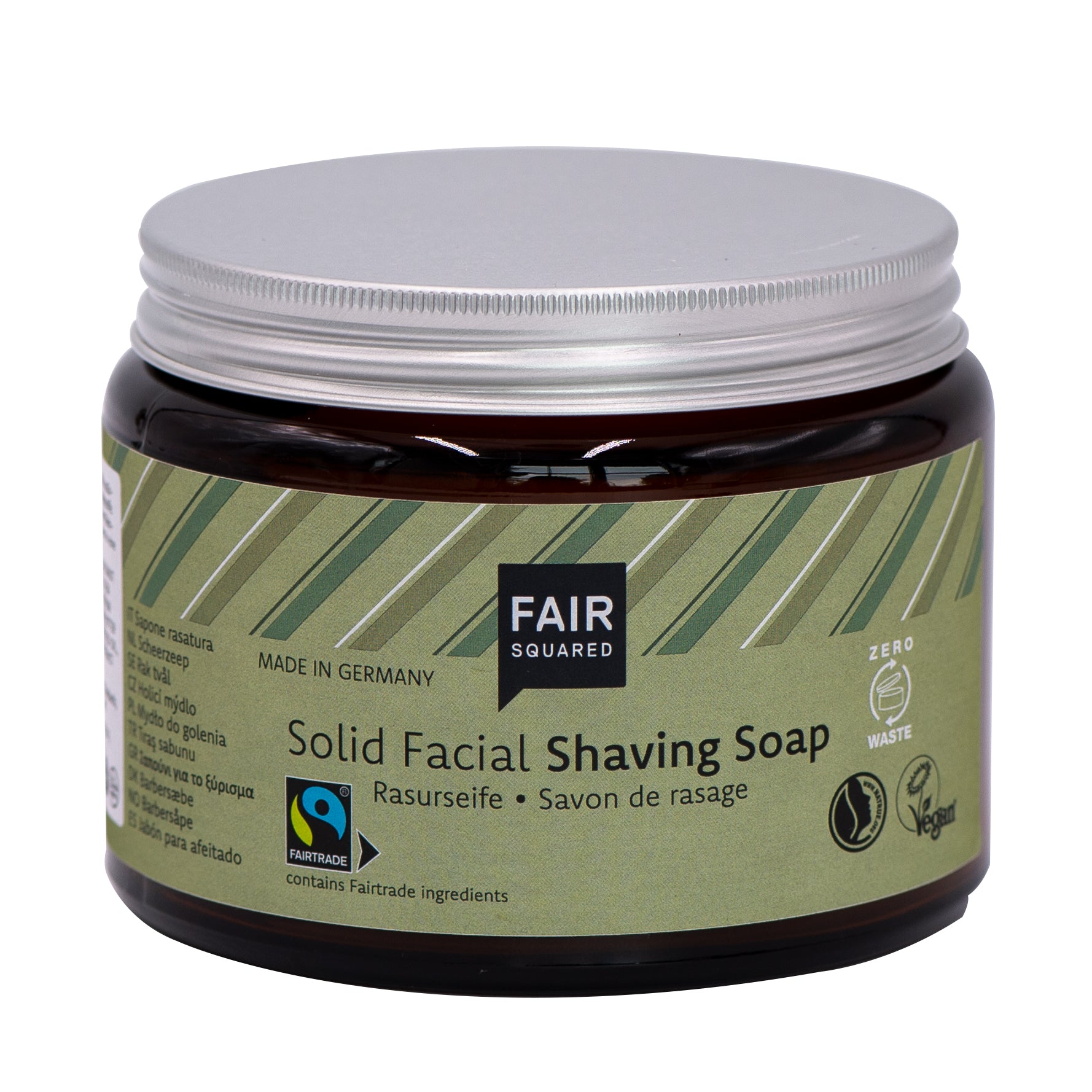 Ein brauner Tiegel mit silbernem Deckel und der Aufschrift FAIR SQUARED Solid Facial Shaving Soap. Das Etikett zeigt Fairtrade-, Vegan- und Zero-Waste-Symbole sowie Text in mehreren Sprachen.