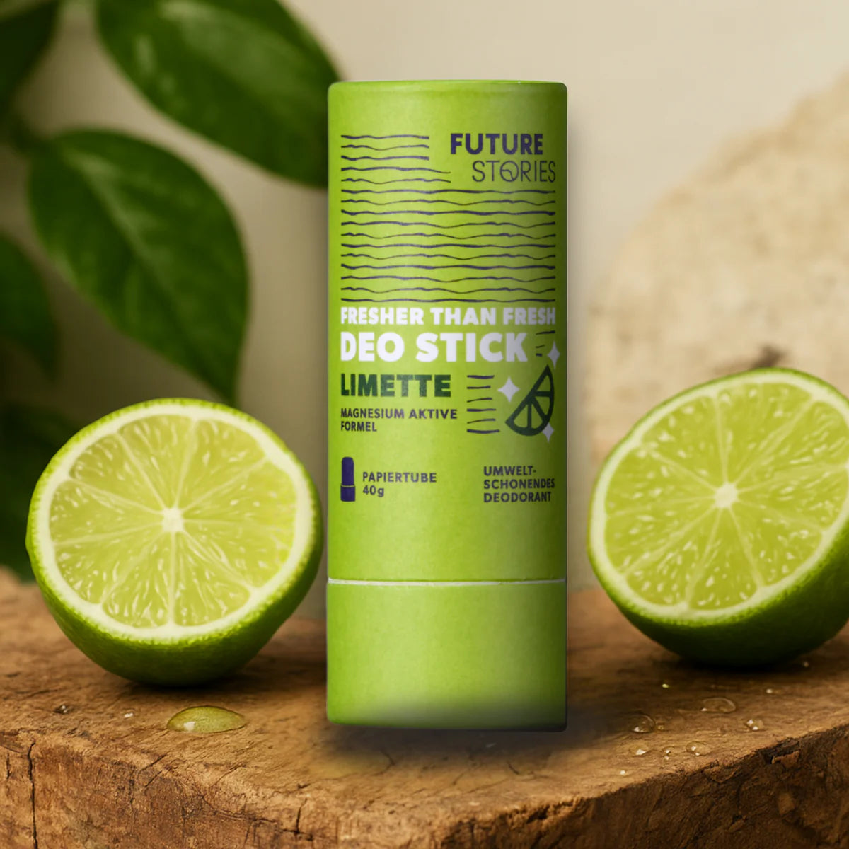 Ein grüner Deo-Stick mit der Aufschrift "Future Stories Deo Stick Limette" steht aufrecht auf einer hölzernen Oberfläche, umgeben von halbierten Limetten und grünen Blättern im Hintergrund. Die Verpackung hebt die umweltfreundlichen Eigenschaften hervor.