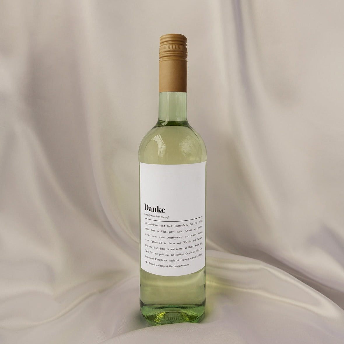 Weißweinflasche mit goldenem Verschluss und Etikett mit der Aufschrift "Danke" vor beigem Hintergrund.