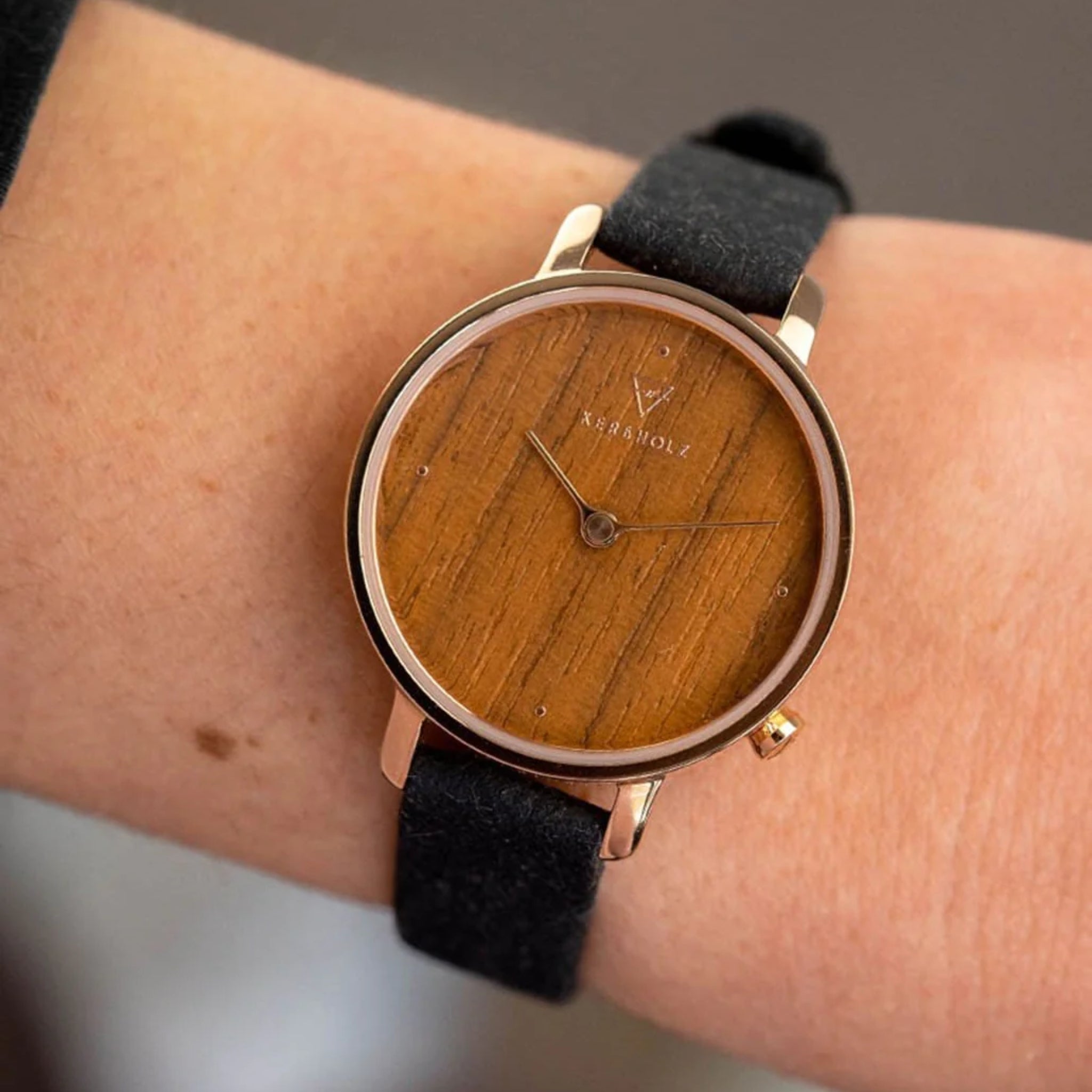 Nahaufnahme einer Armbanduhr mit Holz-Zifferblatt und schwarzem Armband auf einem Handgelenk.