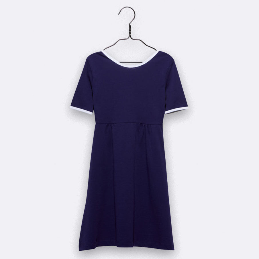 Ein kurzärmeliges, knielanges, marineblaues Kleid mit weißem Besatz an den Ärmeln und am Halsausschnitt, das auf einem schwarzen Bügel vor einem schlichten hellgrauen Hintergrund hängt.
