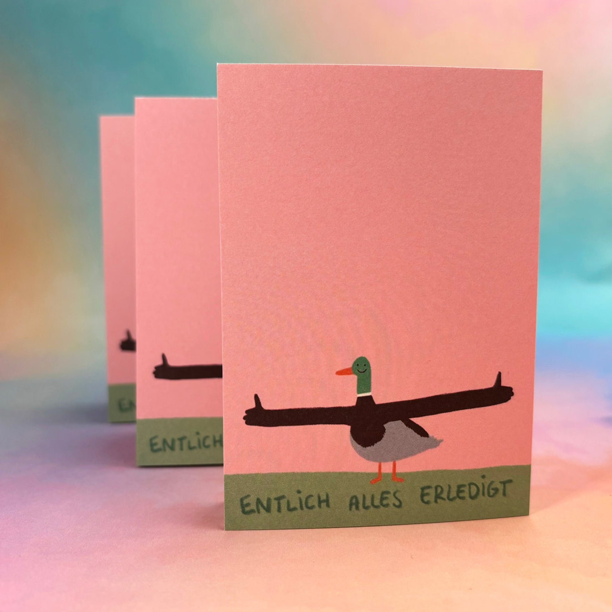 Drei Karten mit einer Zeichnung einer Ente mit ausgestreckten Armen und dem Text "Endlich alles erledigt" auf rosa Hintergrund.