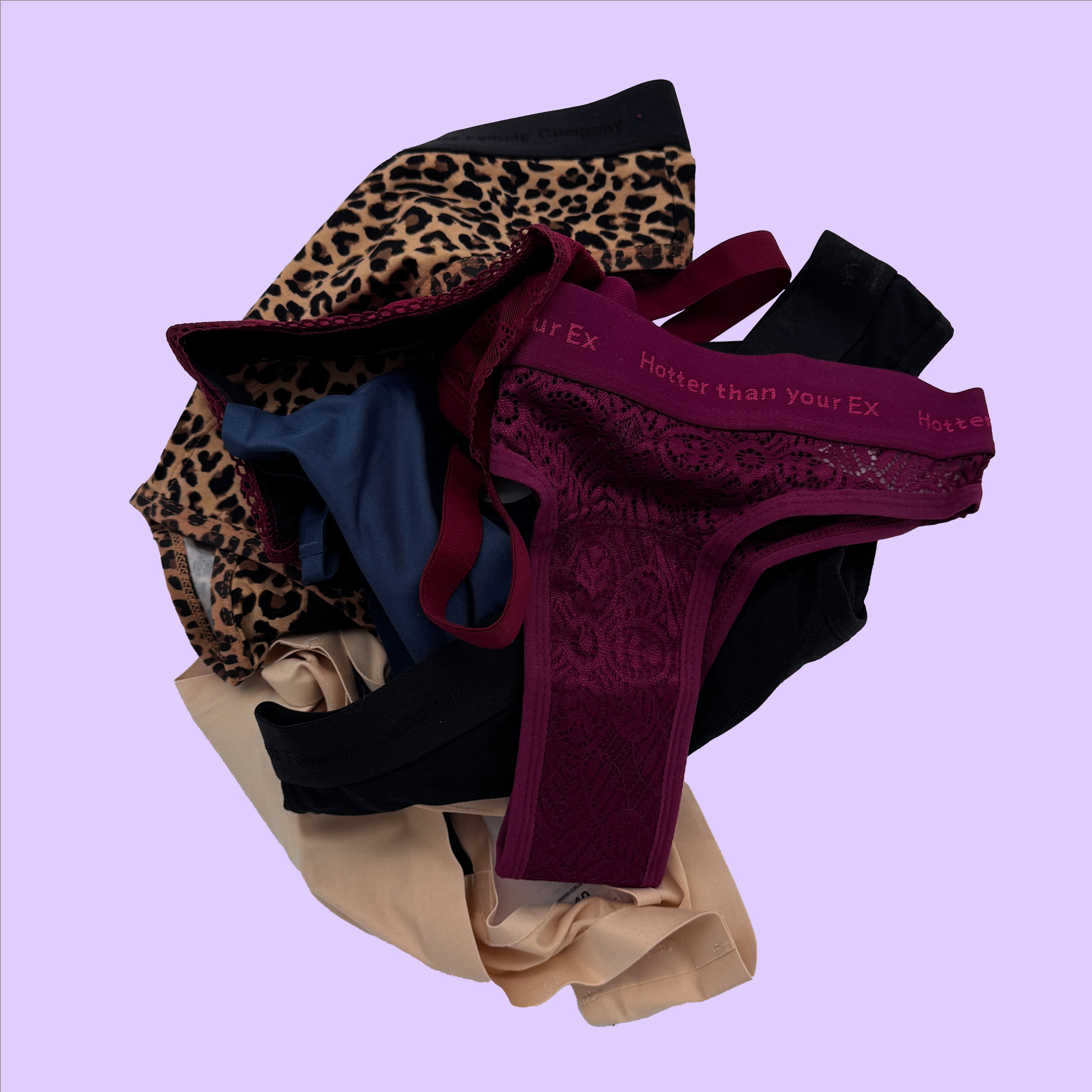 Ein Stapel bunter Unterhosen, darunter Leopardenmuster, schwarze, beige und weinrote Designs, auf lila Hintergrund.