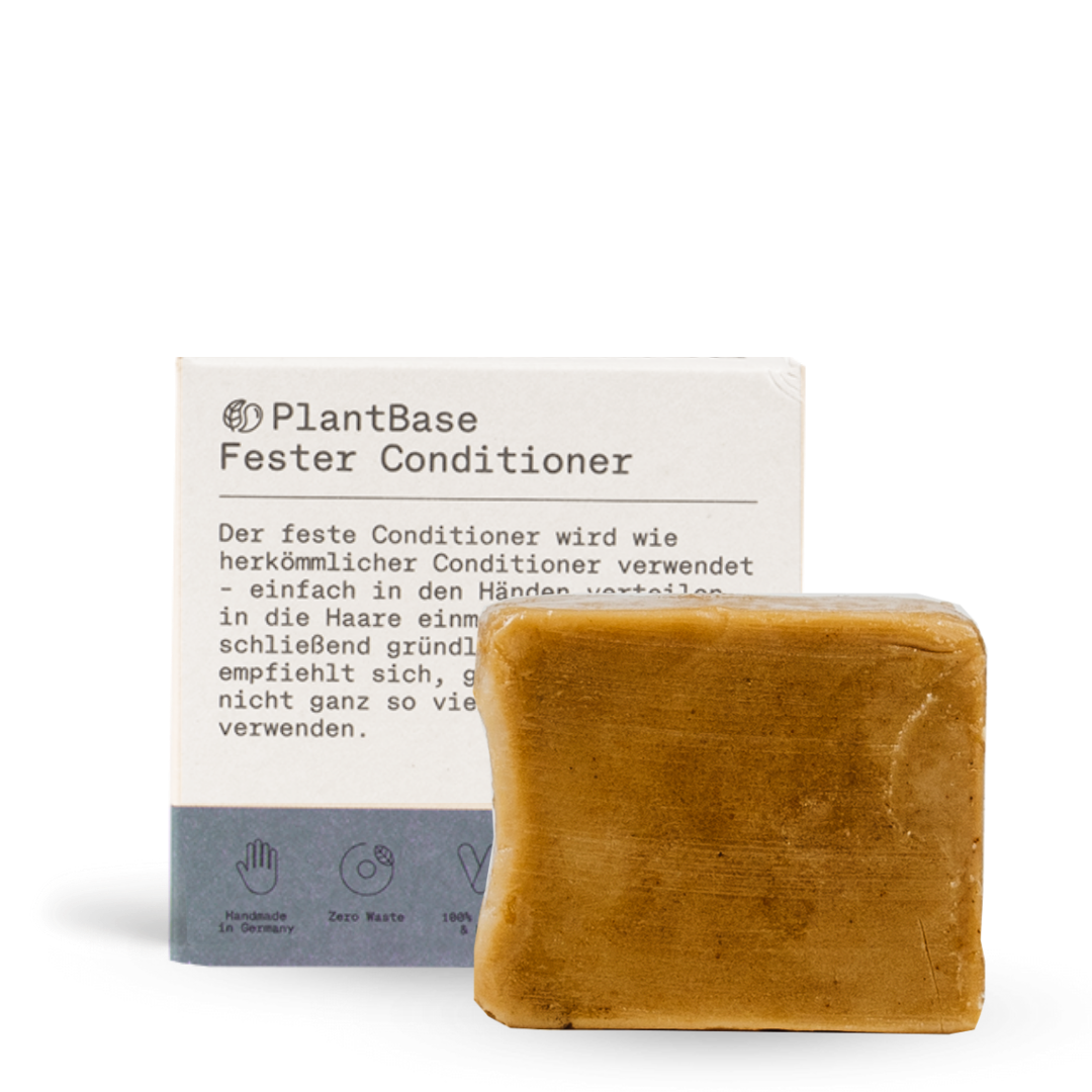 Ein brauner, fester Conditioner-Riegel steht vor seiner Verpackung, die mit der Aufschrift PlantBase Fester Conditioner und den Symbolen für handgemacht, abfallfrei und vegan versehen ist.