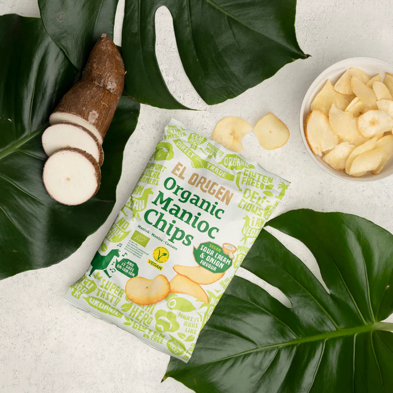 Packet von organischen Maniok-Chips mit geschnittenem Maniok und einer Schüssel Chips, auf tropischen Blättern platziert.
