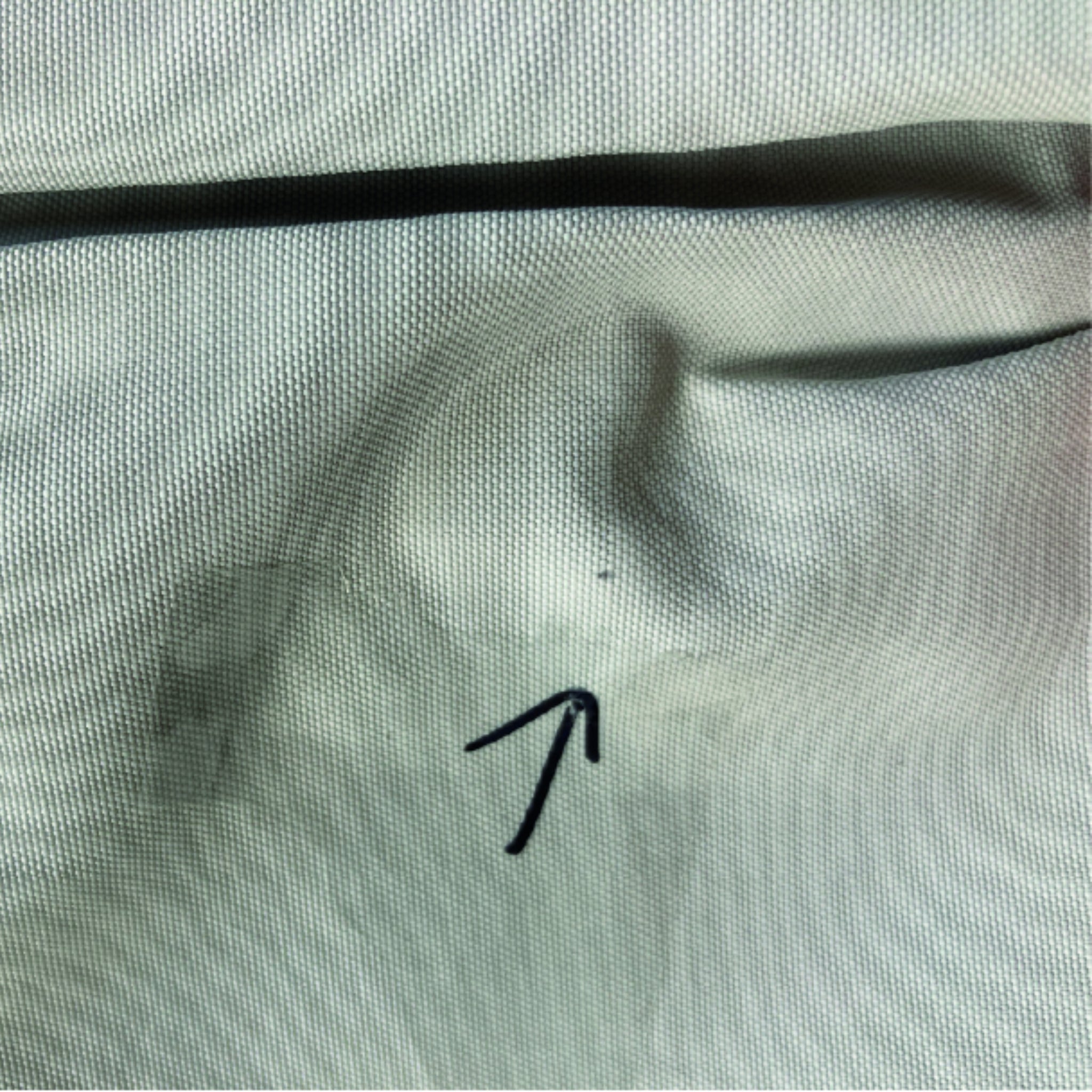 Nahaufnahme eines Stoffes mit einem schwarzen Pfeil, der auf einen kleinen Punkt zeigt.