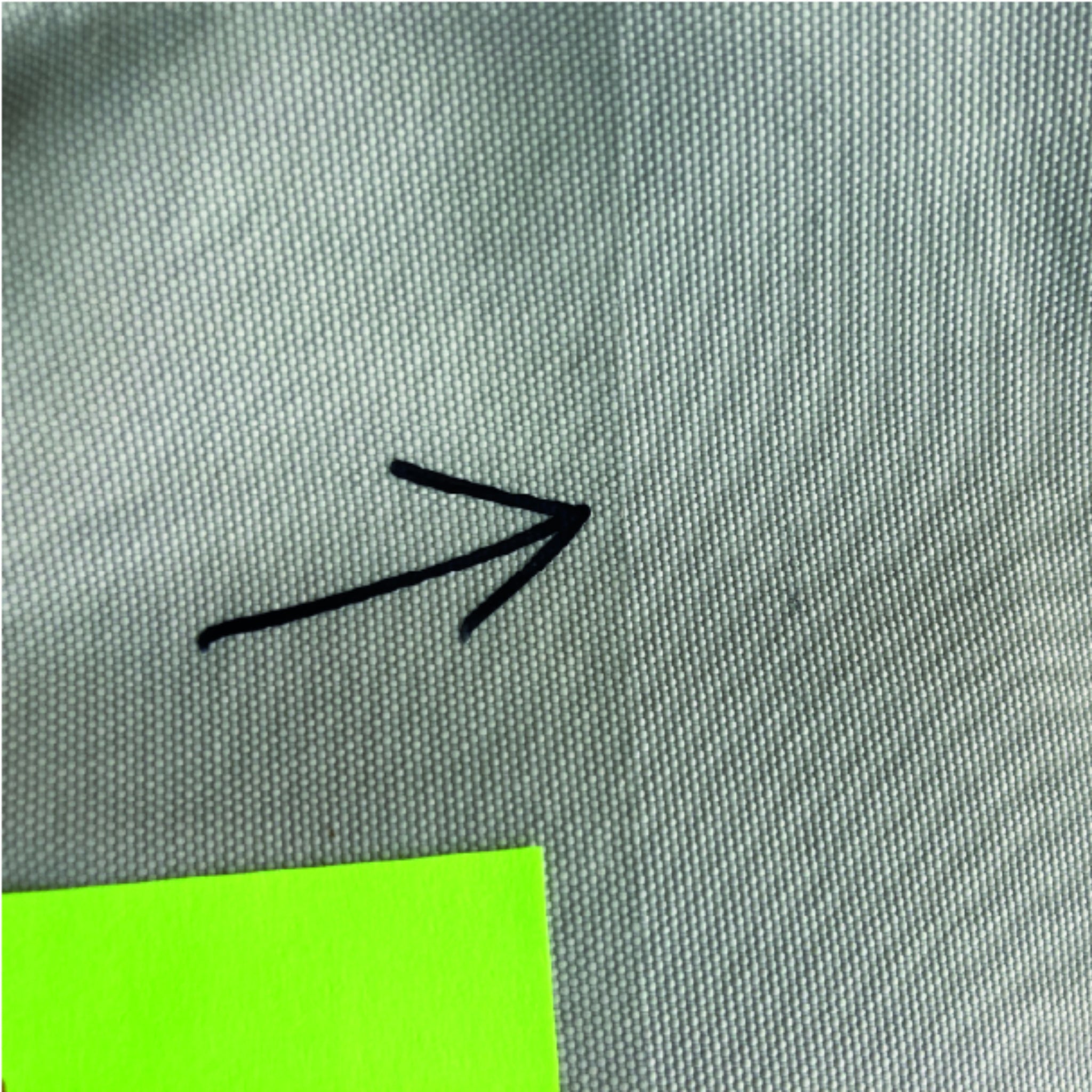 Schwarzer Pfeil auf grauem Stoff, der auf etwas links unten zeigt, neben einem hellgrünen Rechteck.