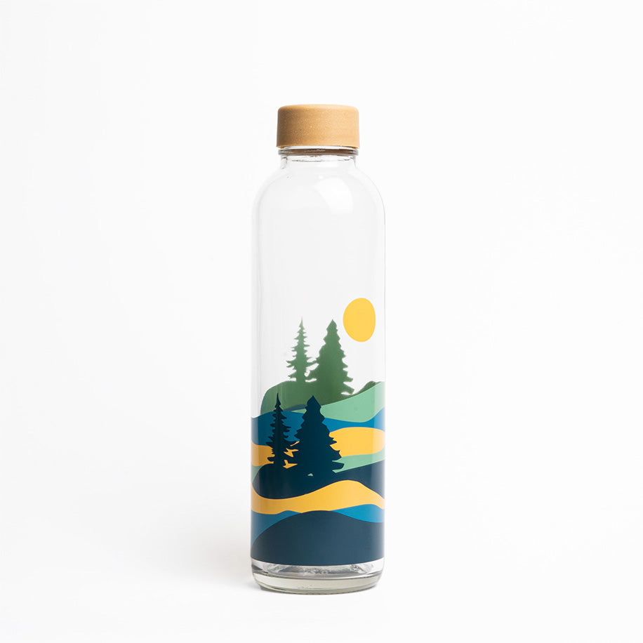 Glasflasche mit Landschaftsillustration: Bäume, gelbe Sonne und Hügel in Blau- und Grüntönen, mit Holzdeckel.