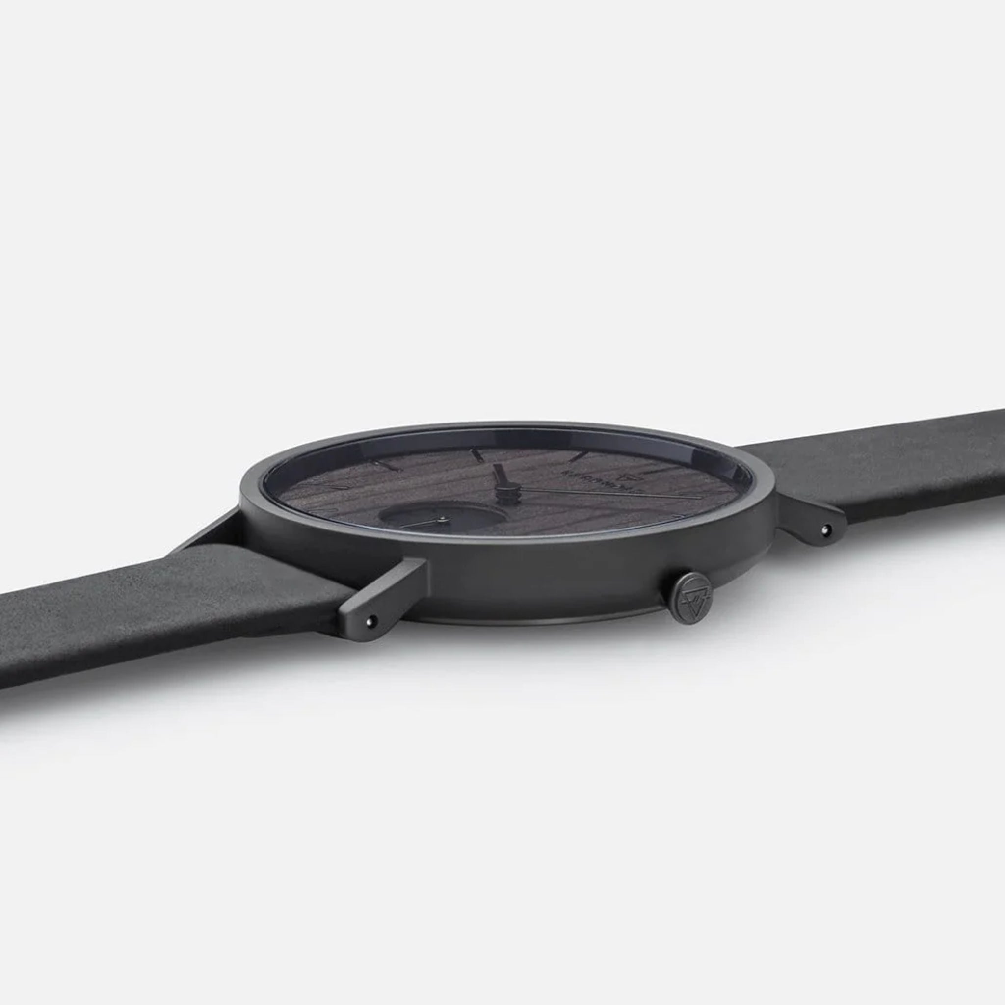 Nahaufnahme einer flachen, schwarzen Armbanduhr mit schwarzem Zifferblatt und schlichtem Design auf hellem Hintergrund.