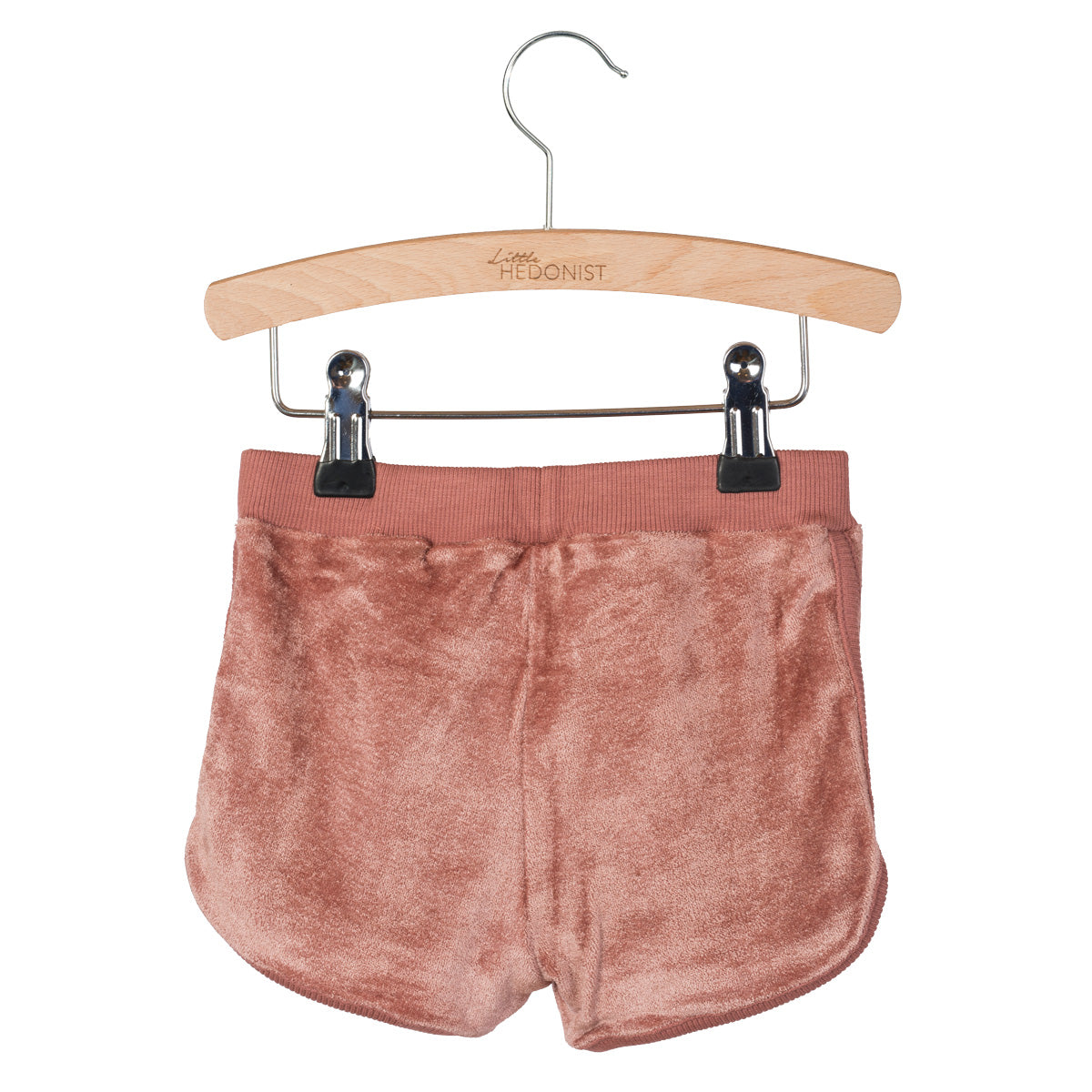 Ein Paar weiche, rosabraune Samtshorts, die auf einem Holzbügel mit Metallklammern vor einem weißen Hintergrund hängen.