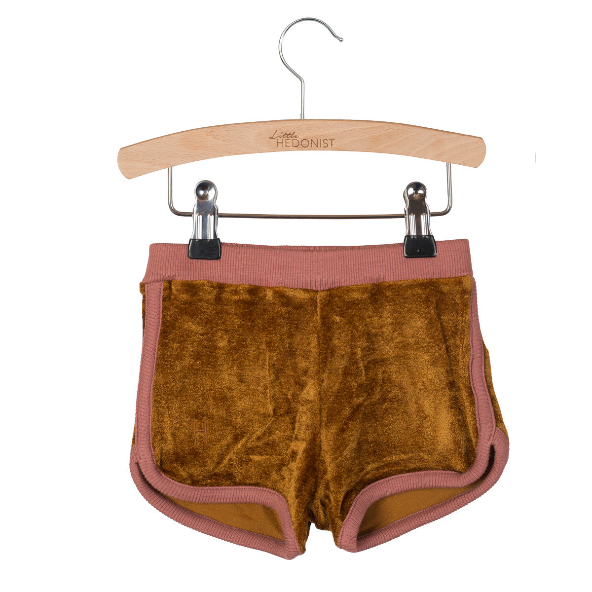 Ein Paar braune Samtshorts mit rosafarbenem Besatz, ausgestellt auf einem Holzbügel mit Metallklammern. Auf dem Bügel ist Little HEDONIST eingraviert. Die Shorts haben einen elastischen Bund und geschwungene Säume.