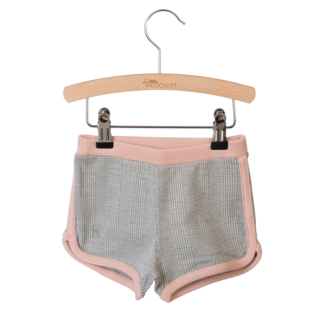 Graue und rosa karierte Kindershorts mit rosafarbenem Rand, aufgehängt an einem Holzbügel mit der Aufschrift Little Hedonist vor einem weißen Hintergrund.