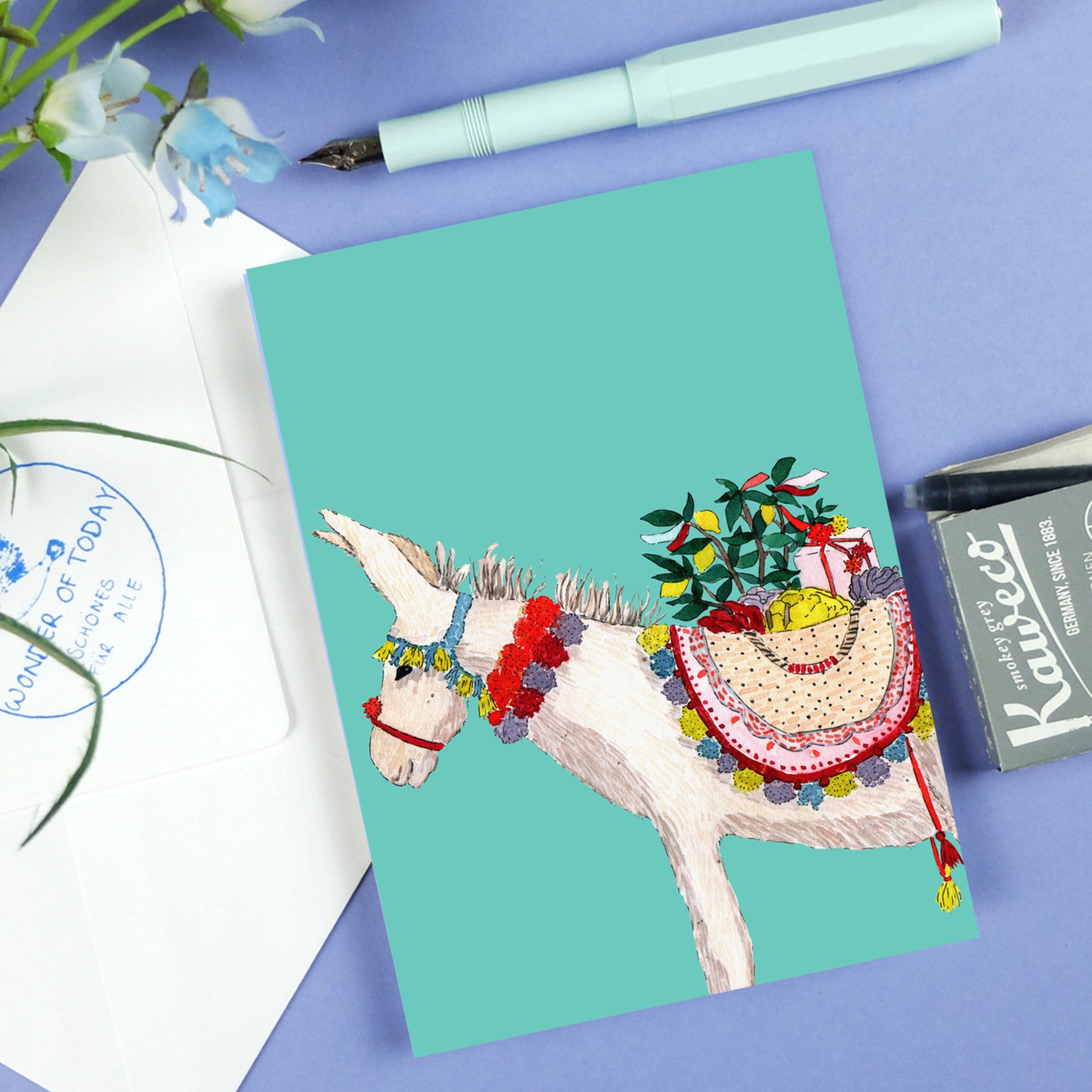 Illustration eines Esels mit buntem Sattel und Körben voller Früchte und Blumen, umgeben von Schreibwaren.