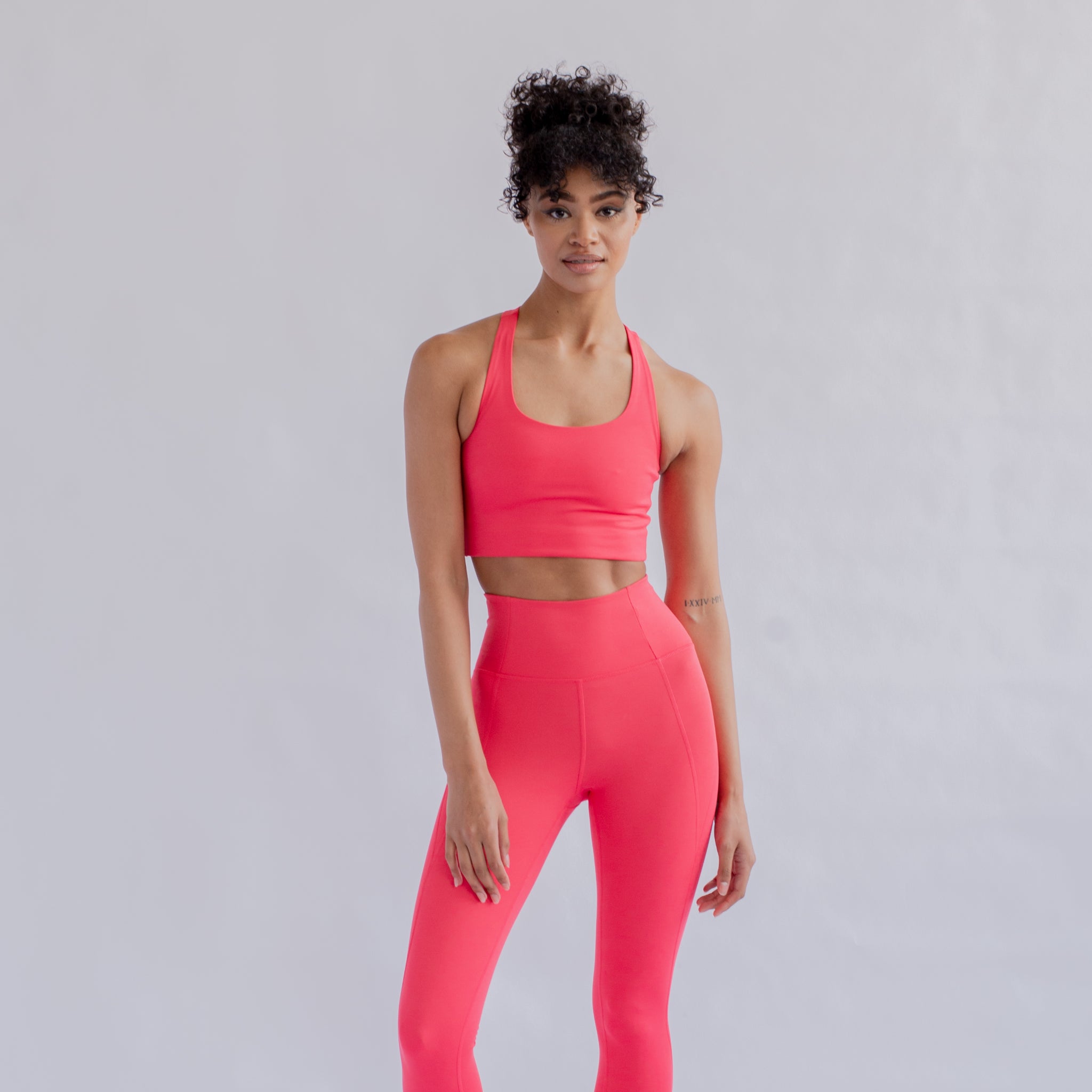 Eine Person in pinker Sportbekleidung vor einem neutralen Hintergrund.