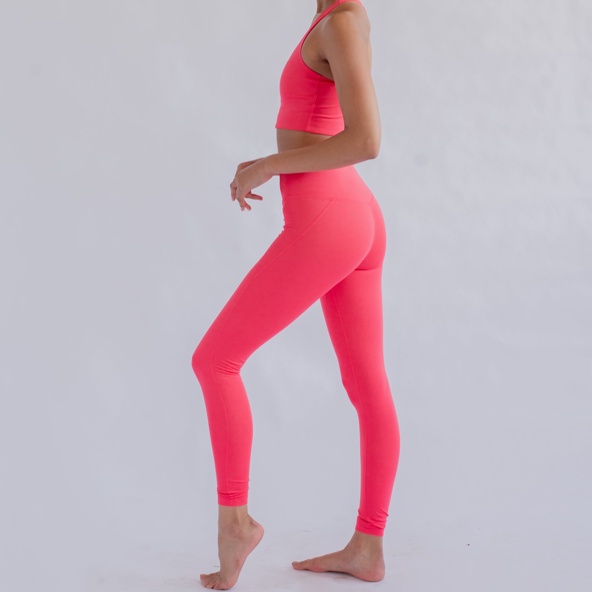 Person im neonpinken Sportoutfit, seitlich stehend vor einem hellen Hintergrund.