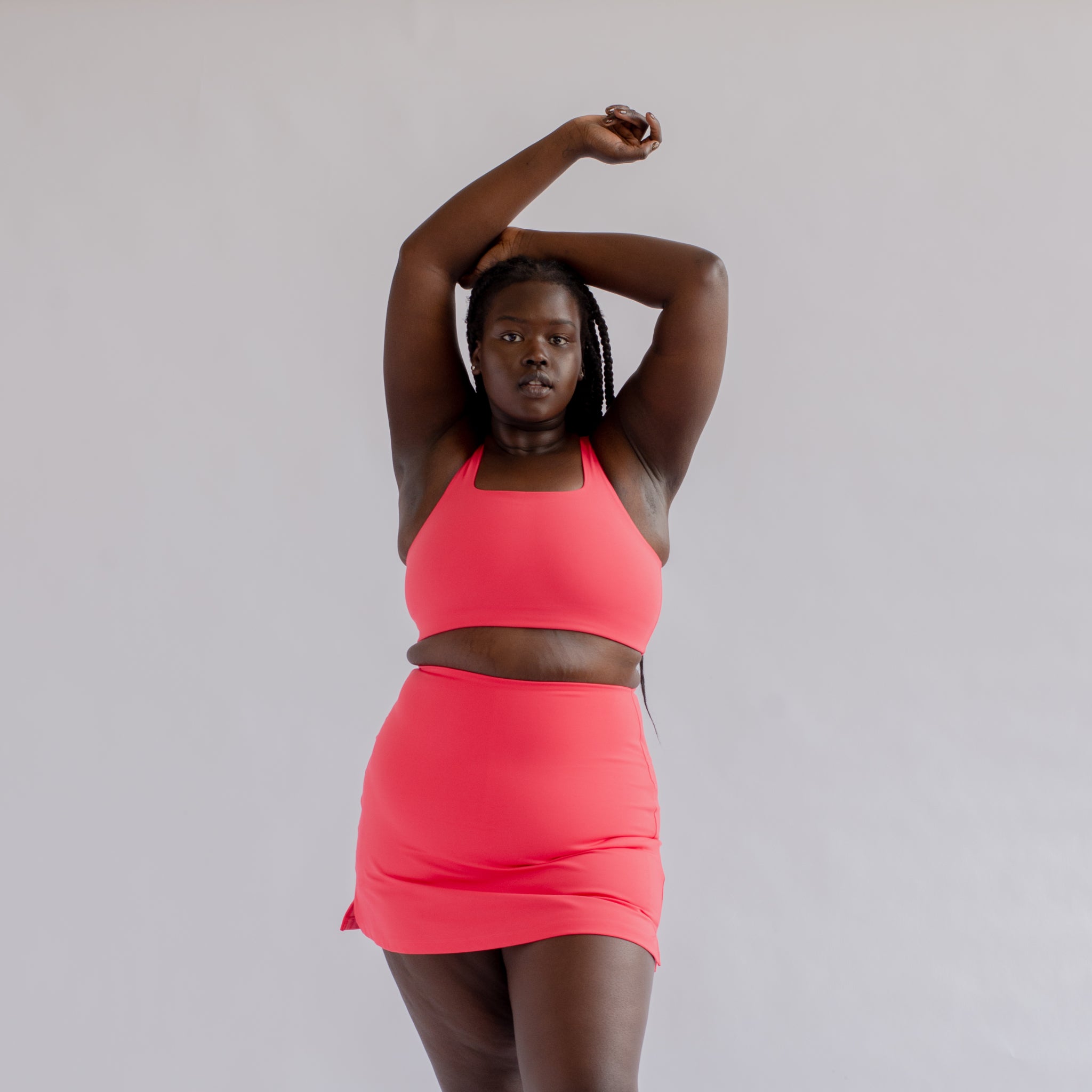 Person in pink athletic wear poses with arms raised against a plain background.