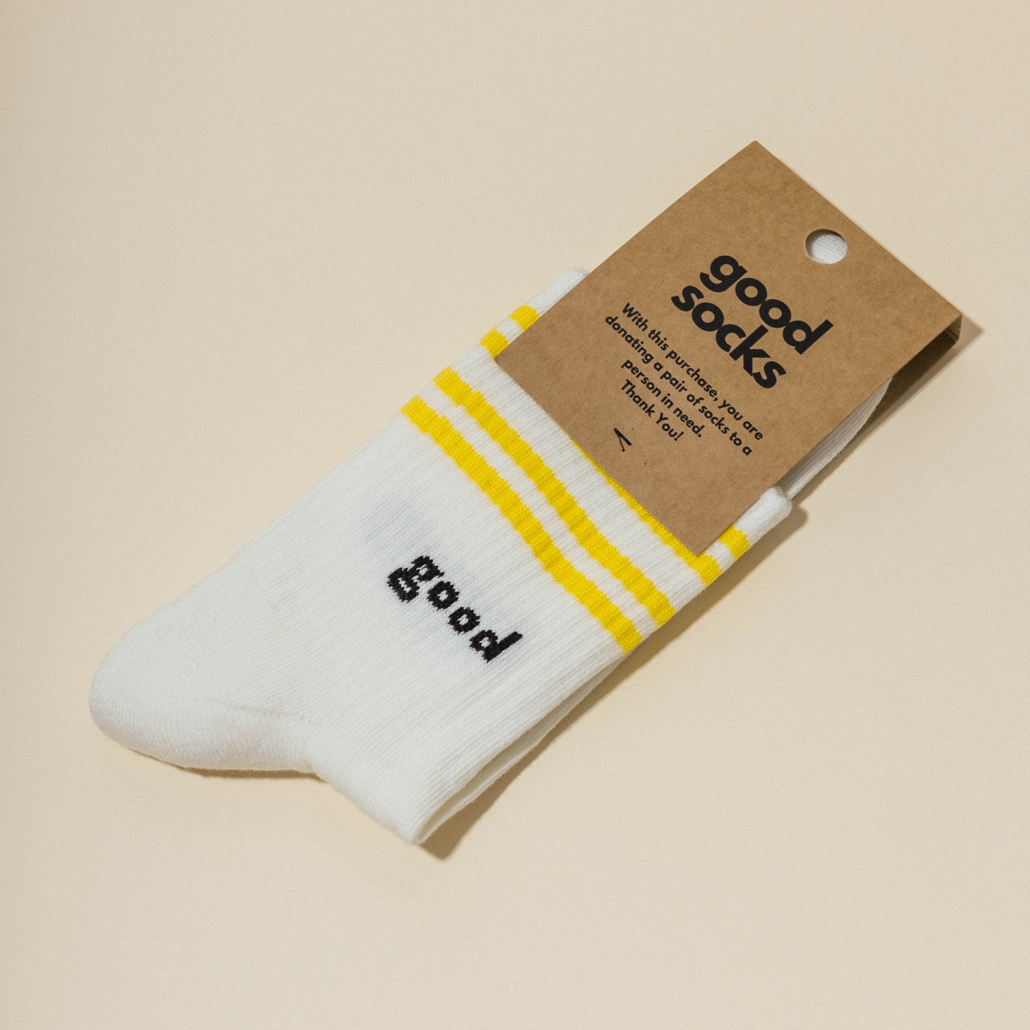 Weiße Socke mit gelben Streifen und der Aufschrift "good" sowie einer braunen Verpackung mit dem Text "good socks".