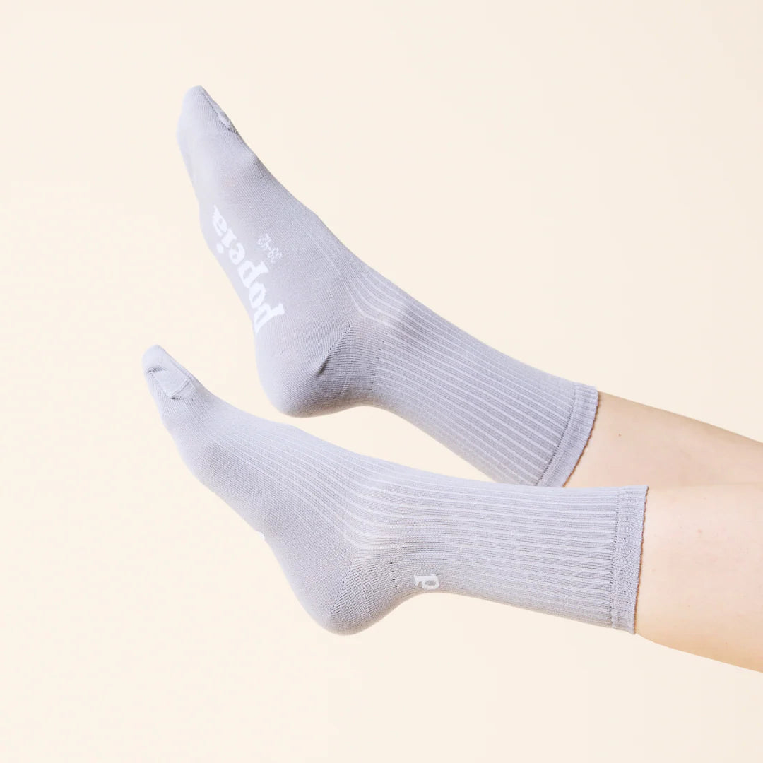 Ein Paar Füße in hellgrauen, gerippten Socken mit weißem Text, die sich von einem hellen Hintergrund abheben.