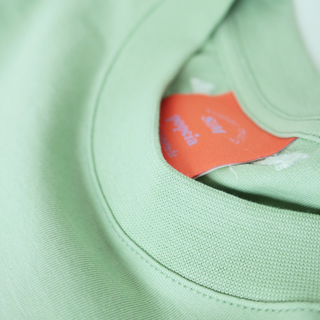 Nahaufnahme eines grünen T-Shirts mit einem orangefarbenen Etikett im Nackenbereich.