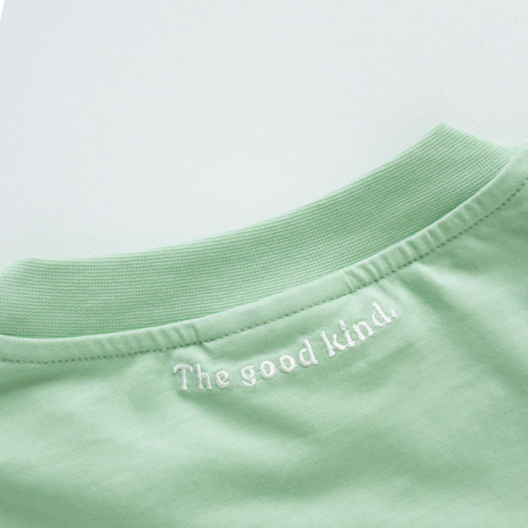 Hinterer Kragenausschnitt eines mintgrünen T-Shirts mit dem gestickten Schriftzug "The good kind." in Weiß.