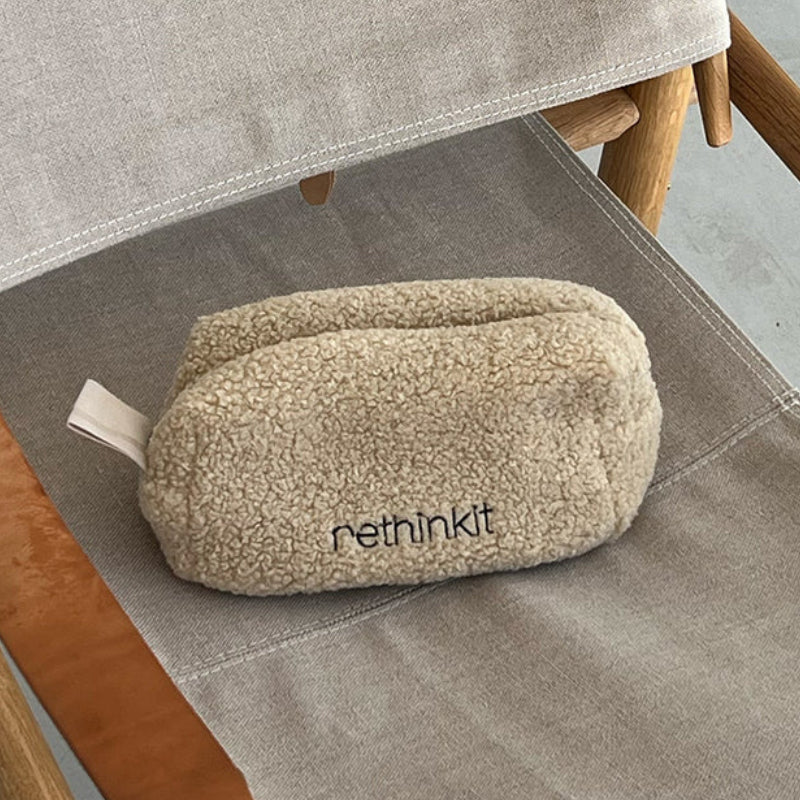 Ein beiger Vliesbeutel mit der Aufschrift rethinkit liegt auf der Sitzfläche eines Klappstuhls aus Segeltuch und Holz neben einem gemusterten Teppich.