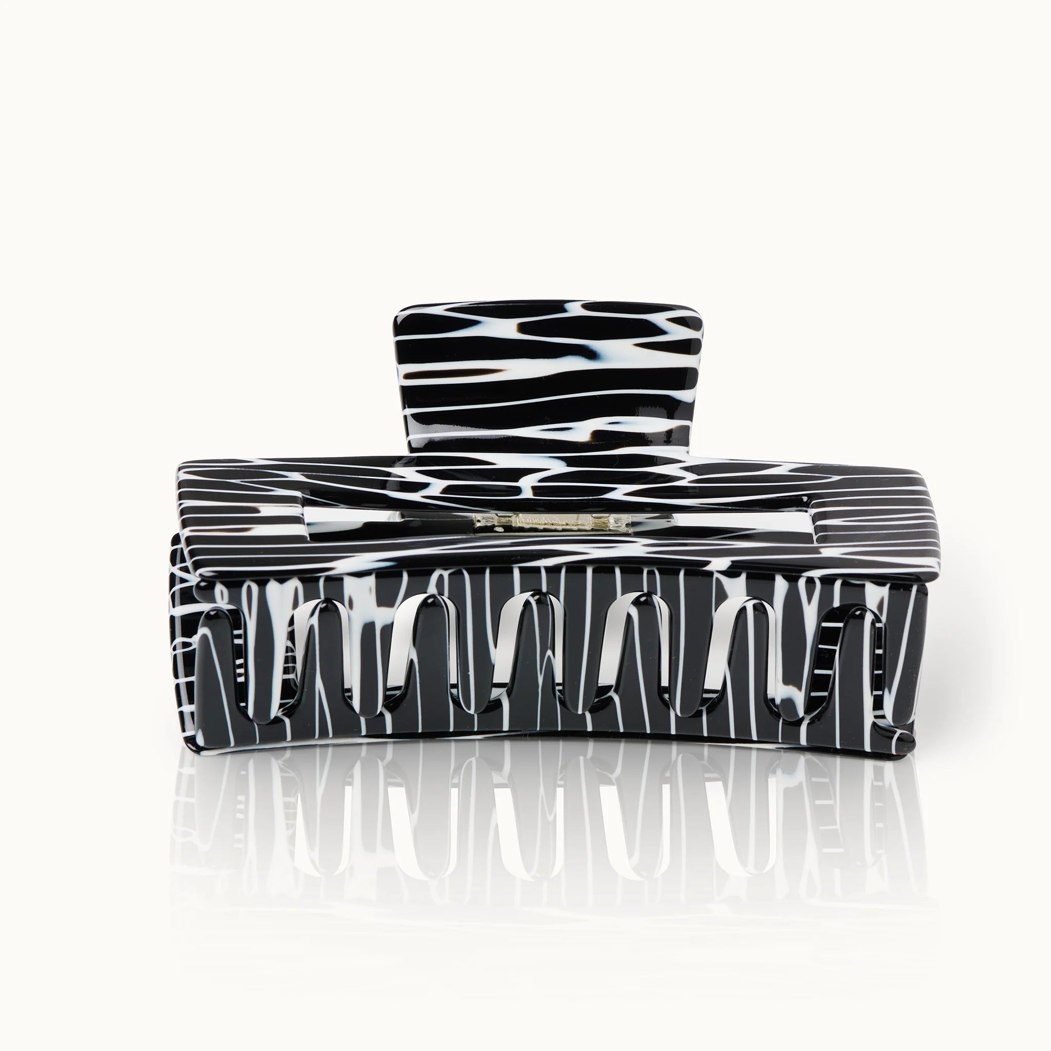 Schwarze und weiße Haarklammer mit gestreiftem Muster, auf einer reflektierenden Oberfläche liegend.