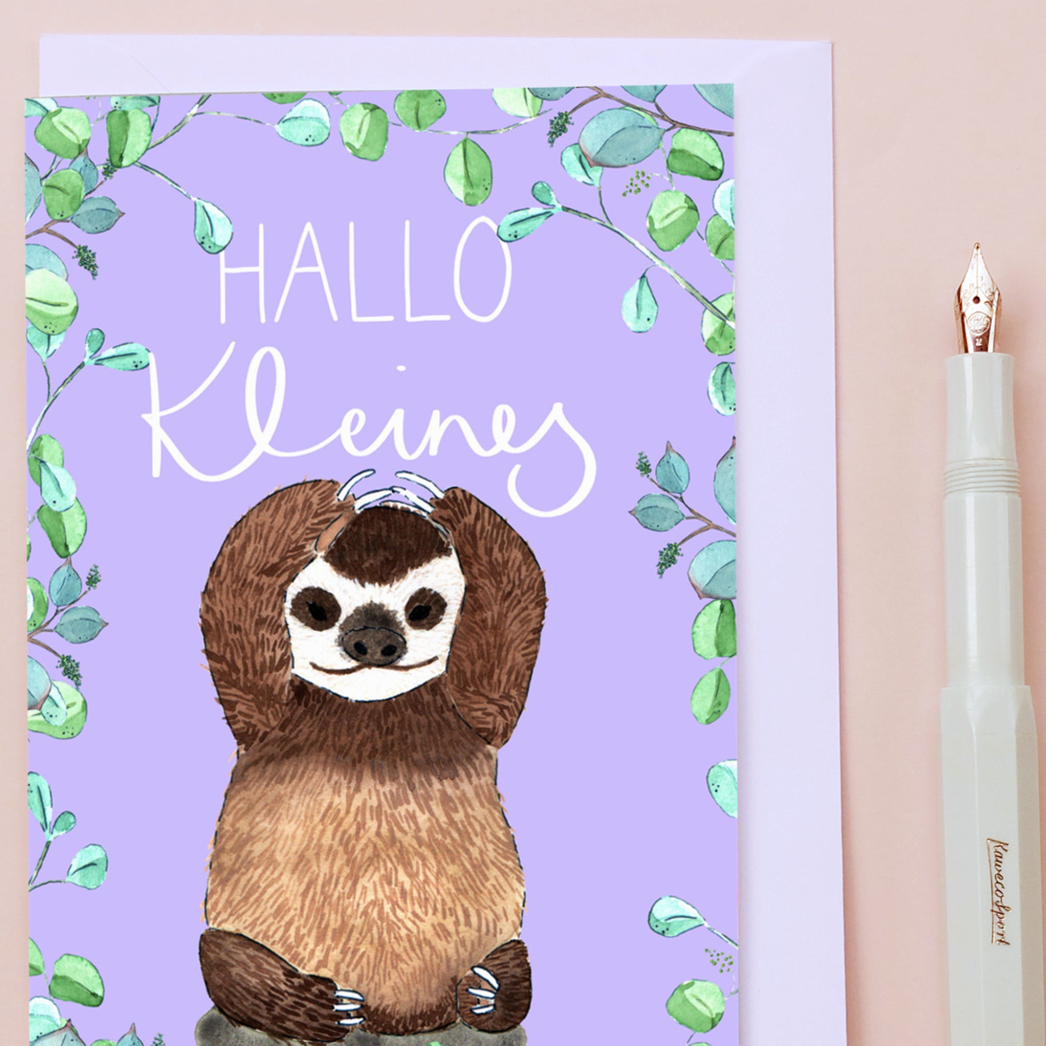 Grußkarte mit einem gezeichneten Faultier vor lila Hintergrund, umgeben von Blättern und der Aufschrift "HALLO Kleine".