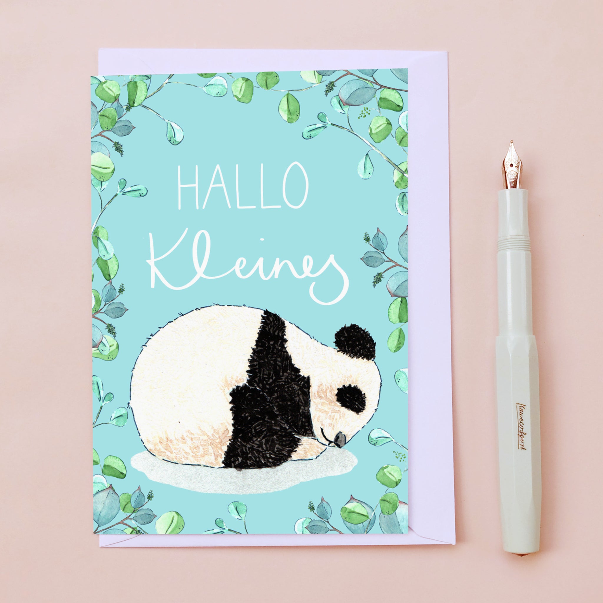 Karte mit schlafendem Panda und "HALLO Kleines" auf hellblauem Hintergrund mit Blattmuster, daneben ein weißer Stift.