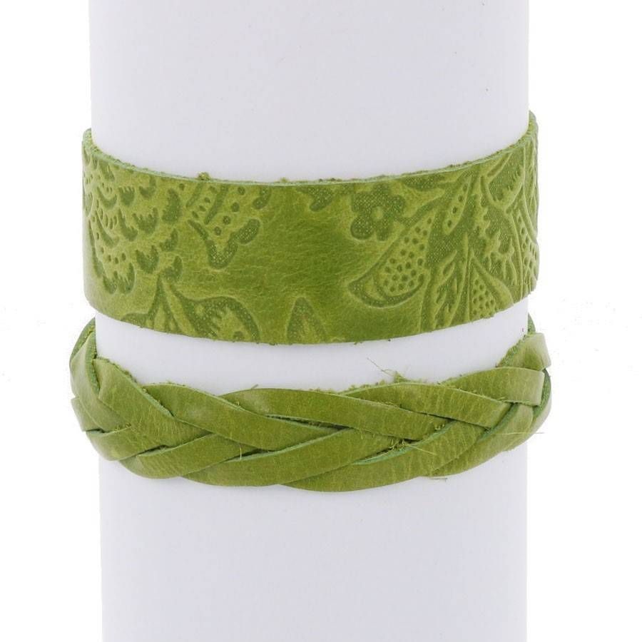 Zwei grüne Lederarmbänder auf einem weißen Display: ein breites mit geprägtem Blumenmuster und ein schmaleres mit einem geflochtenen Muster.