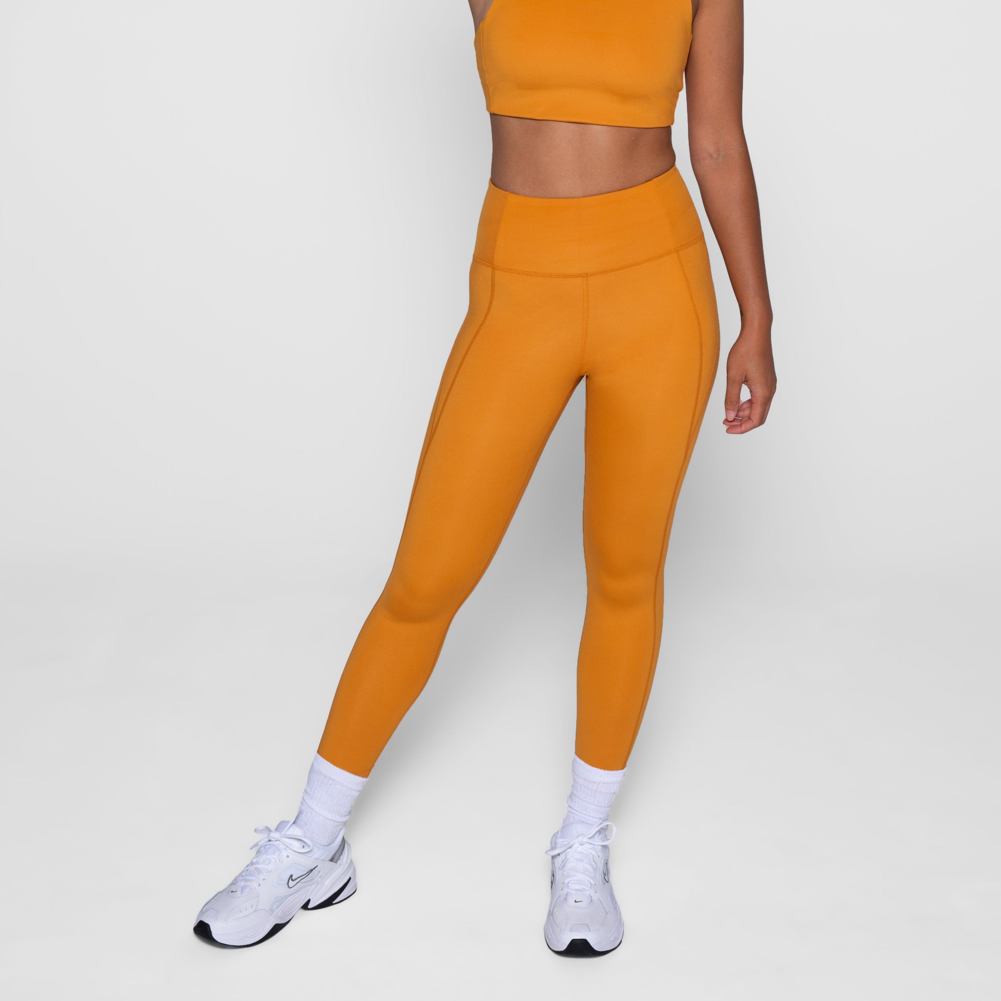 Person trägt ein oranges Sportset mit weißen Turnschuhen auf weißem Hintergrund.