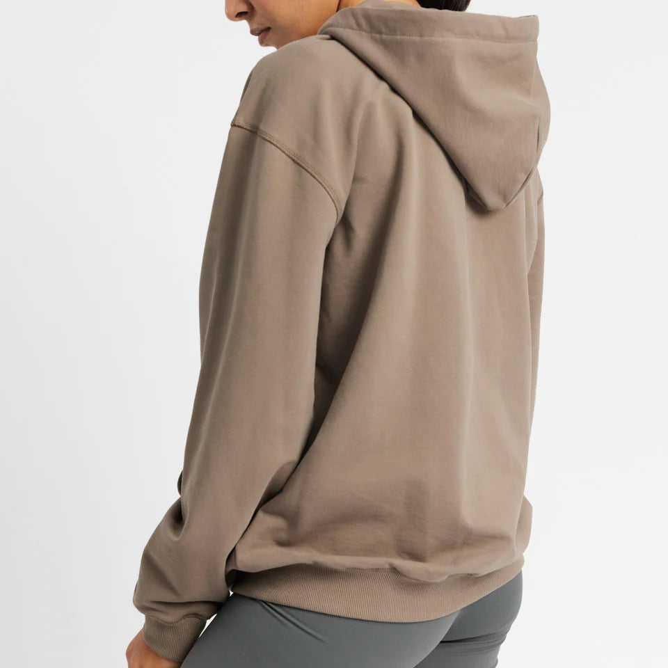 Person mit braunem Hoodie und grauer Hose, die zur Seite blickt.