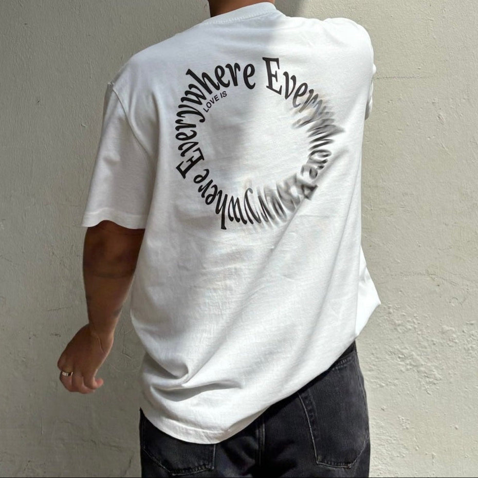 Person trägt ein weißes T-Shirt mit der Aufschrift "Love is everywhere" in spiralförmigem Text auf dem Rücken.