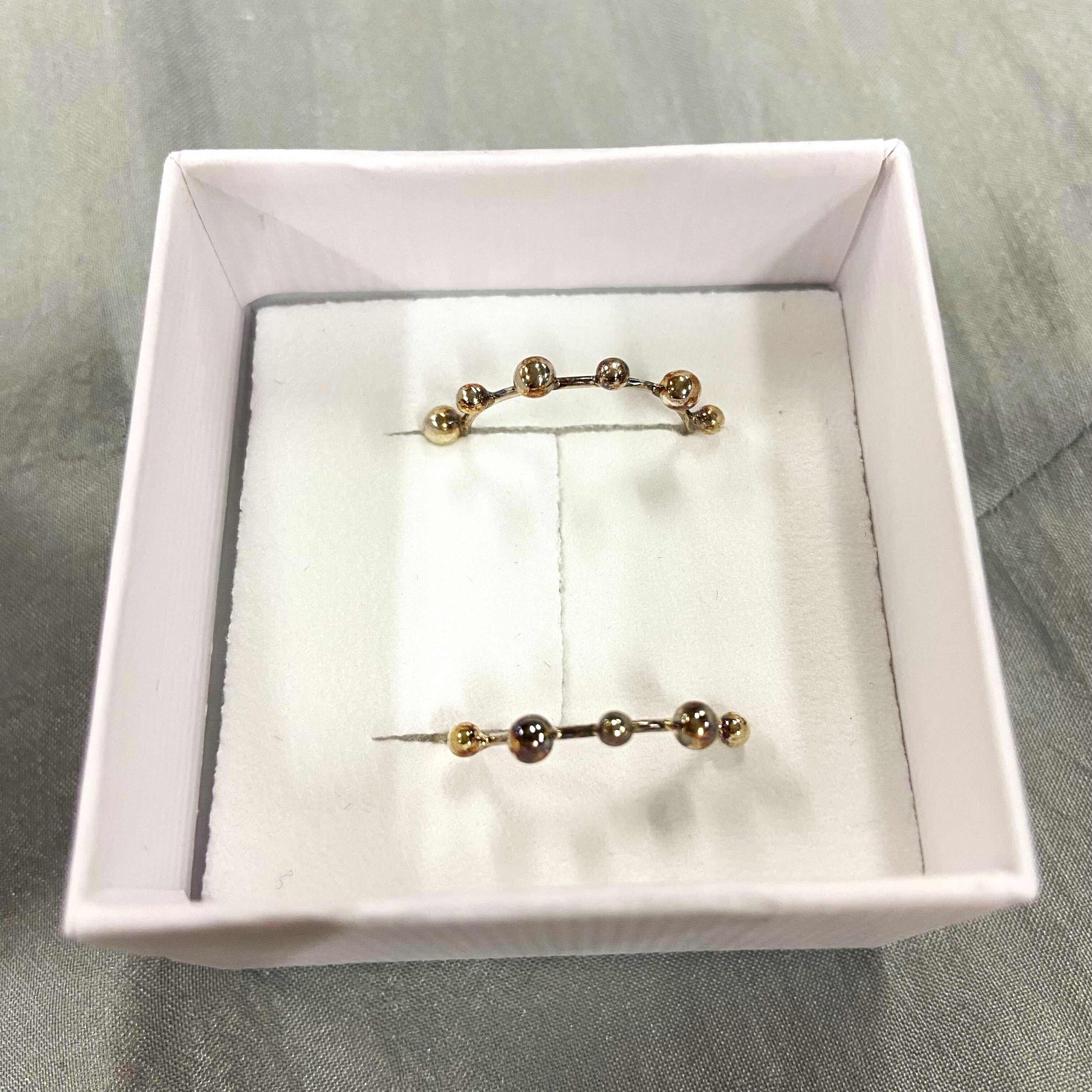 Zwei goldene Ohrstecker mit kugelförmigen Verzierungen liegen in einer weißen Schmuckschatulle auf grauem Hintergrund.