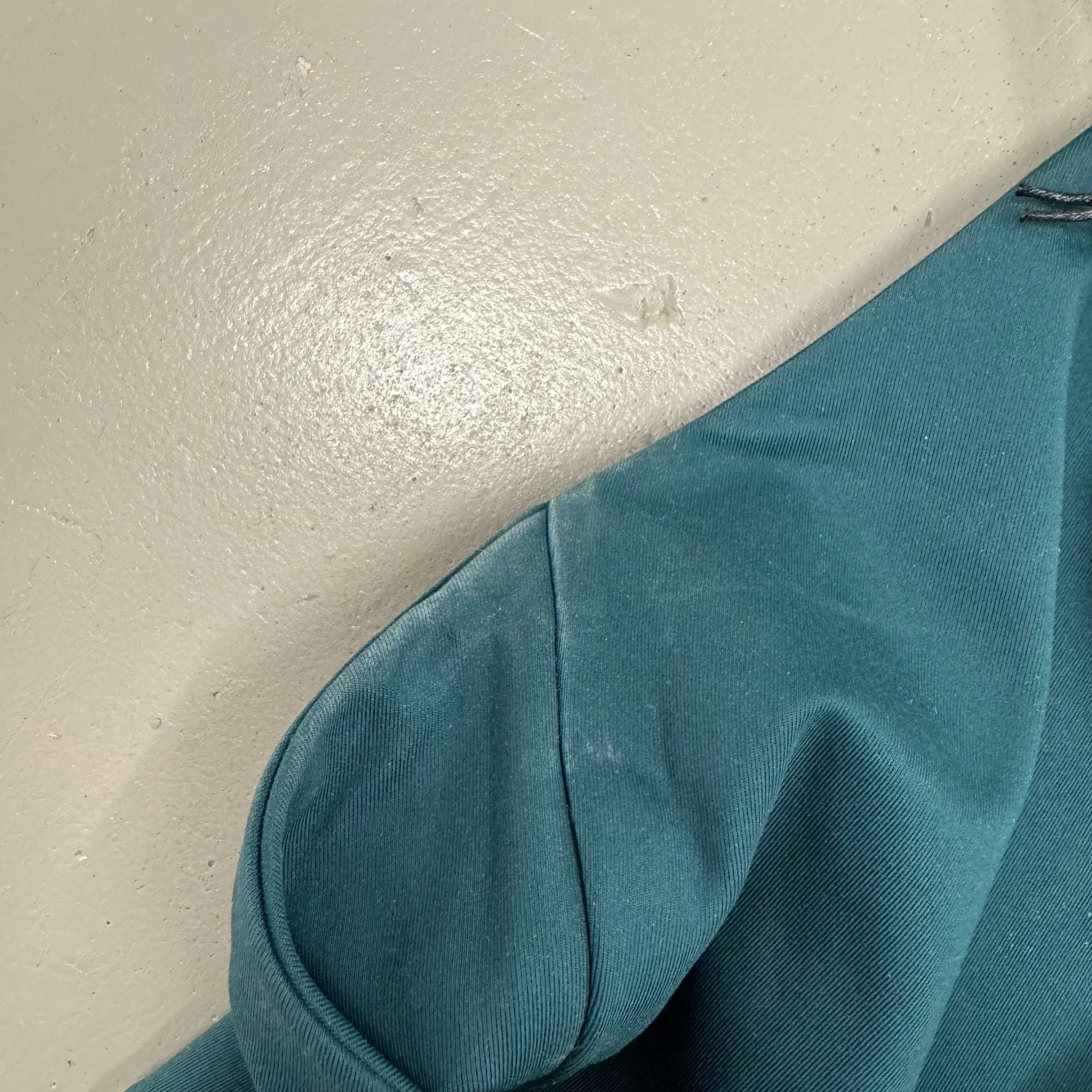 Ein grünes Kleidungsstück liegt auf einem grauen, strukturierten Boden.