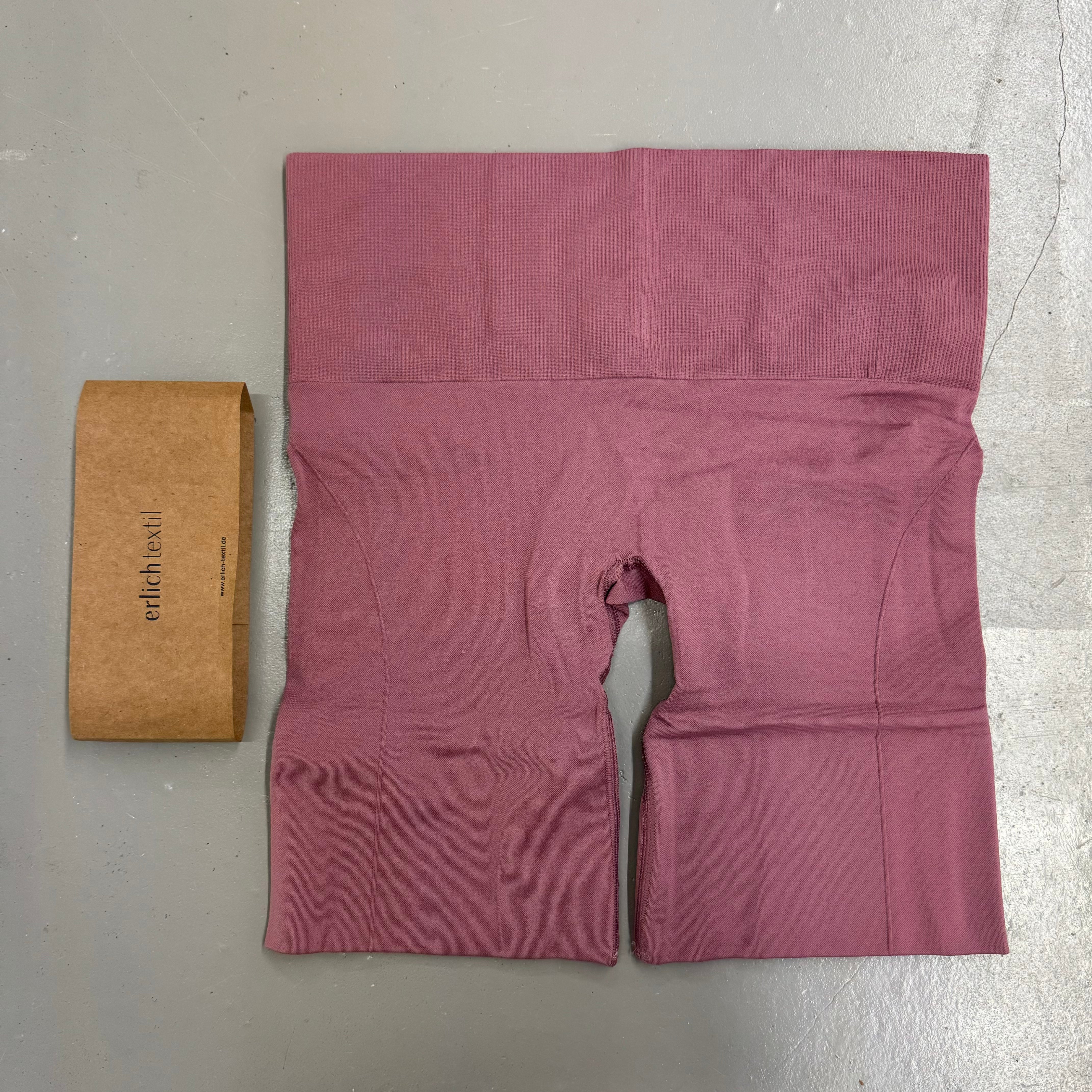 Rote Radlerhose und braune Verpackung mit dem Aufdruck "erlich textil" auf einem grauen Hintergrund.