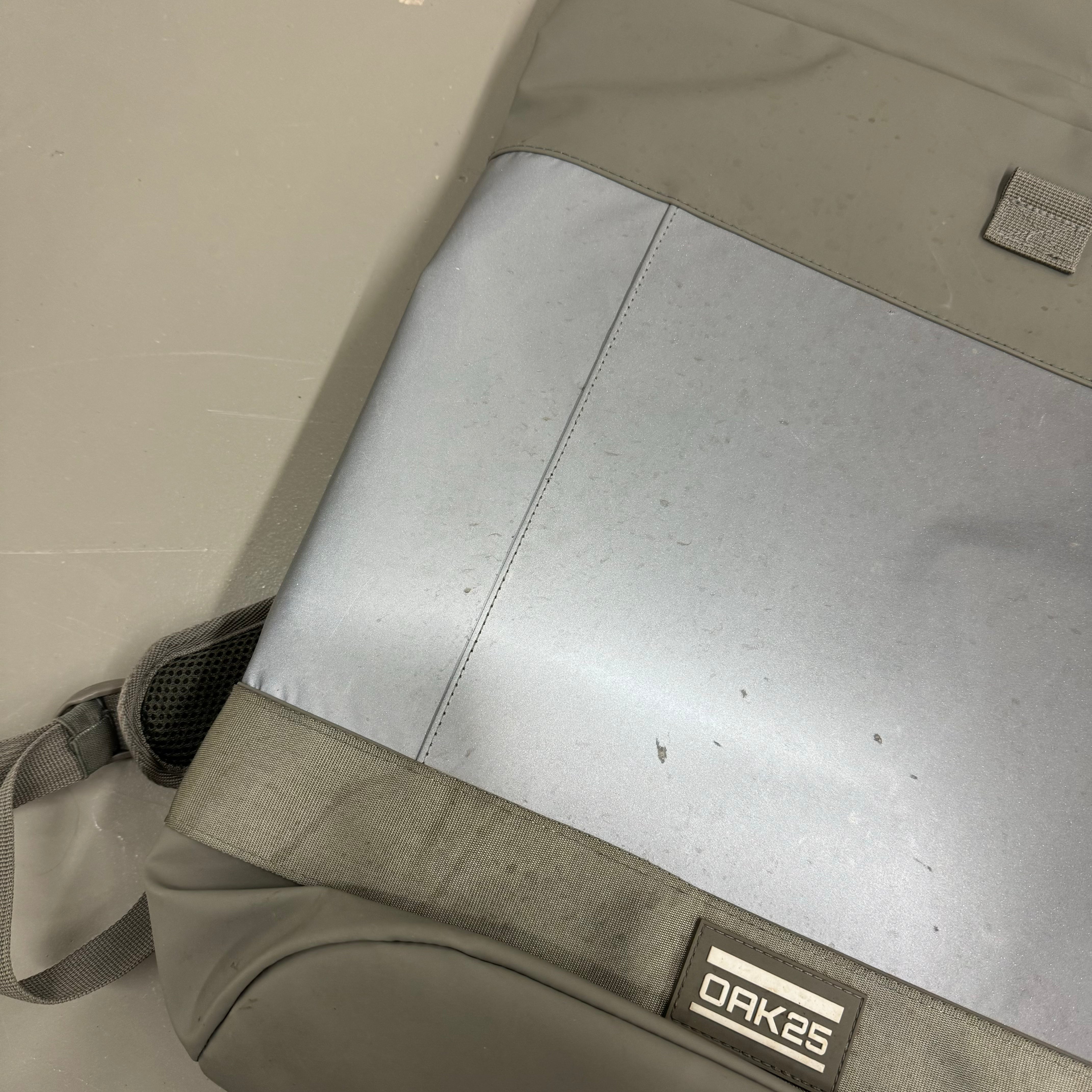 Grauer Rucksack mit Logo "OAK 25" auf einem grauen Hintergrund, leicht schmutzig.