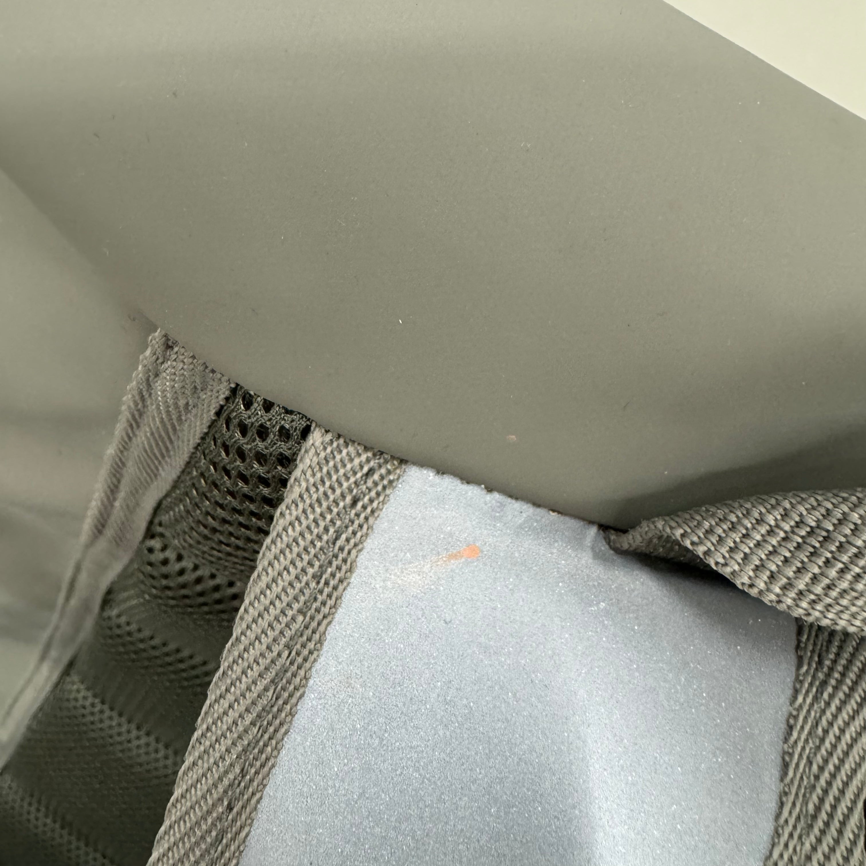 Nahaufnahme eines grauen Trageriemens mit Netz und Stoffstruktur an einem Rucksack oder einer Tasche.