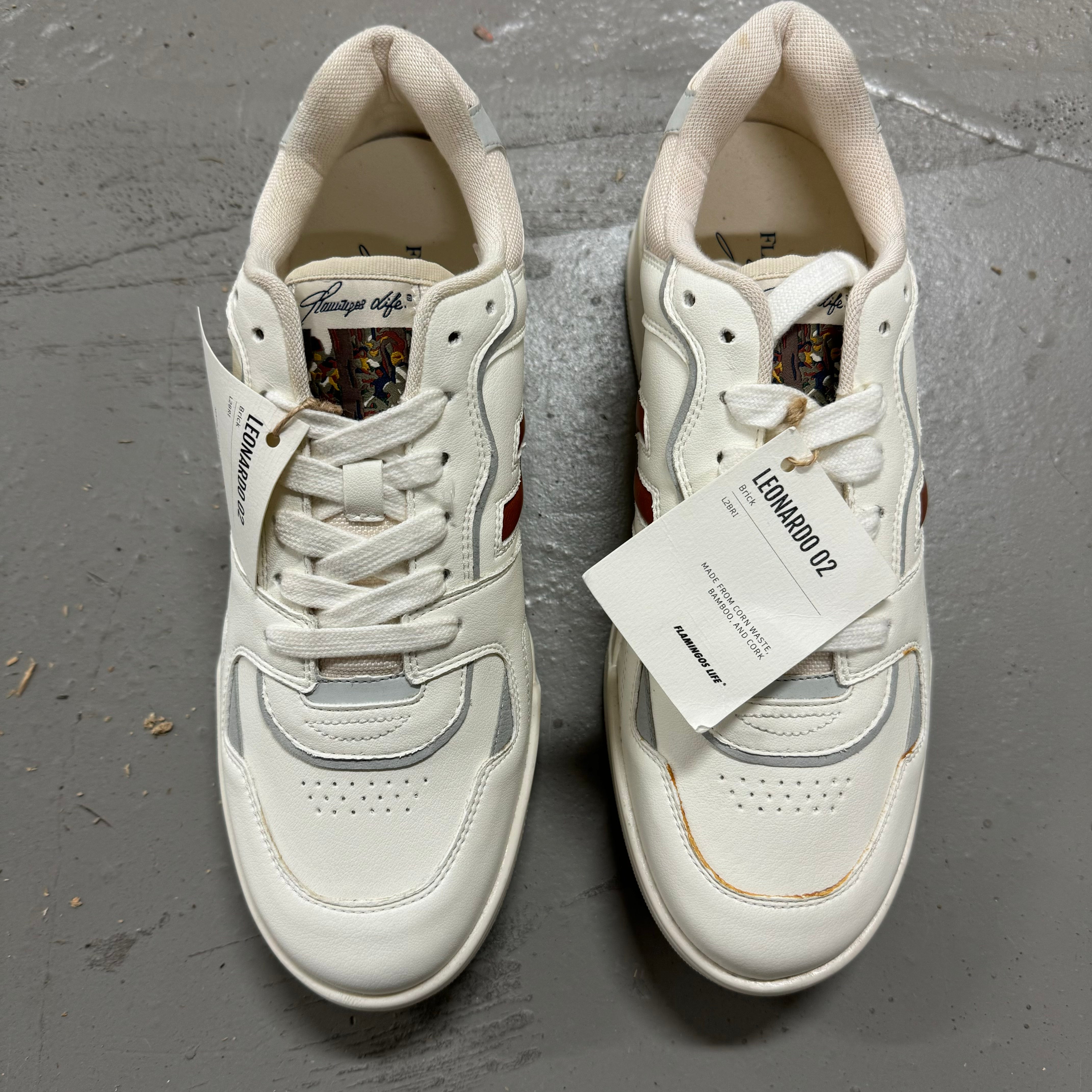 Weiße Sneaker mit charakteristischen Designs und Etiketten, auf grauem Boden stehend.