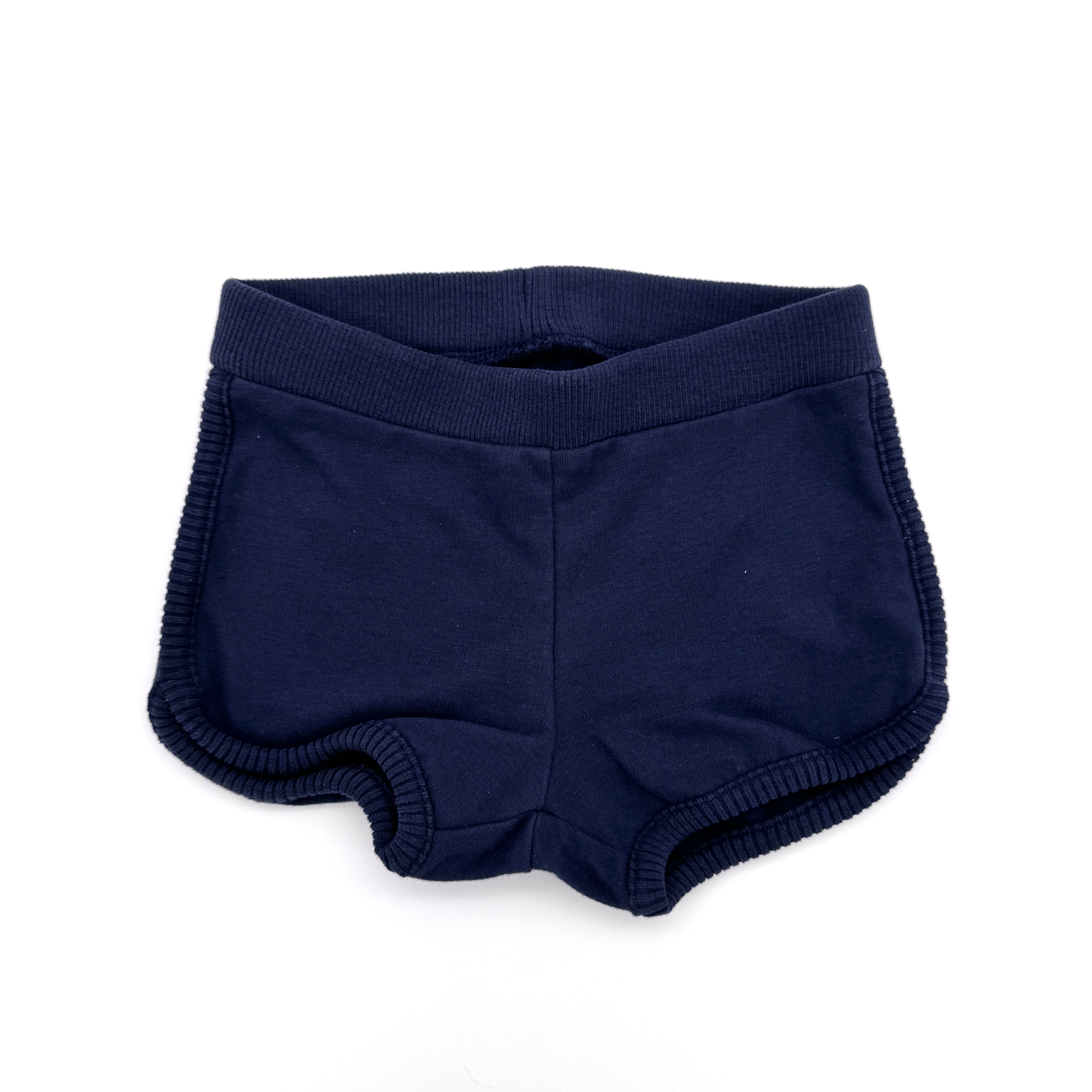 Ein Paar marineblaue Sportshorts mit elastischem Bund und gerippten Abschlüssen, flach auf weißem Hintergrund.