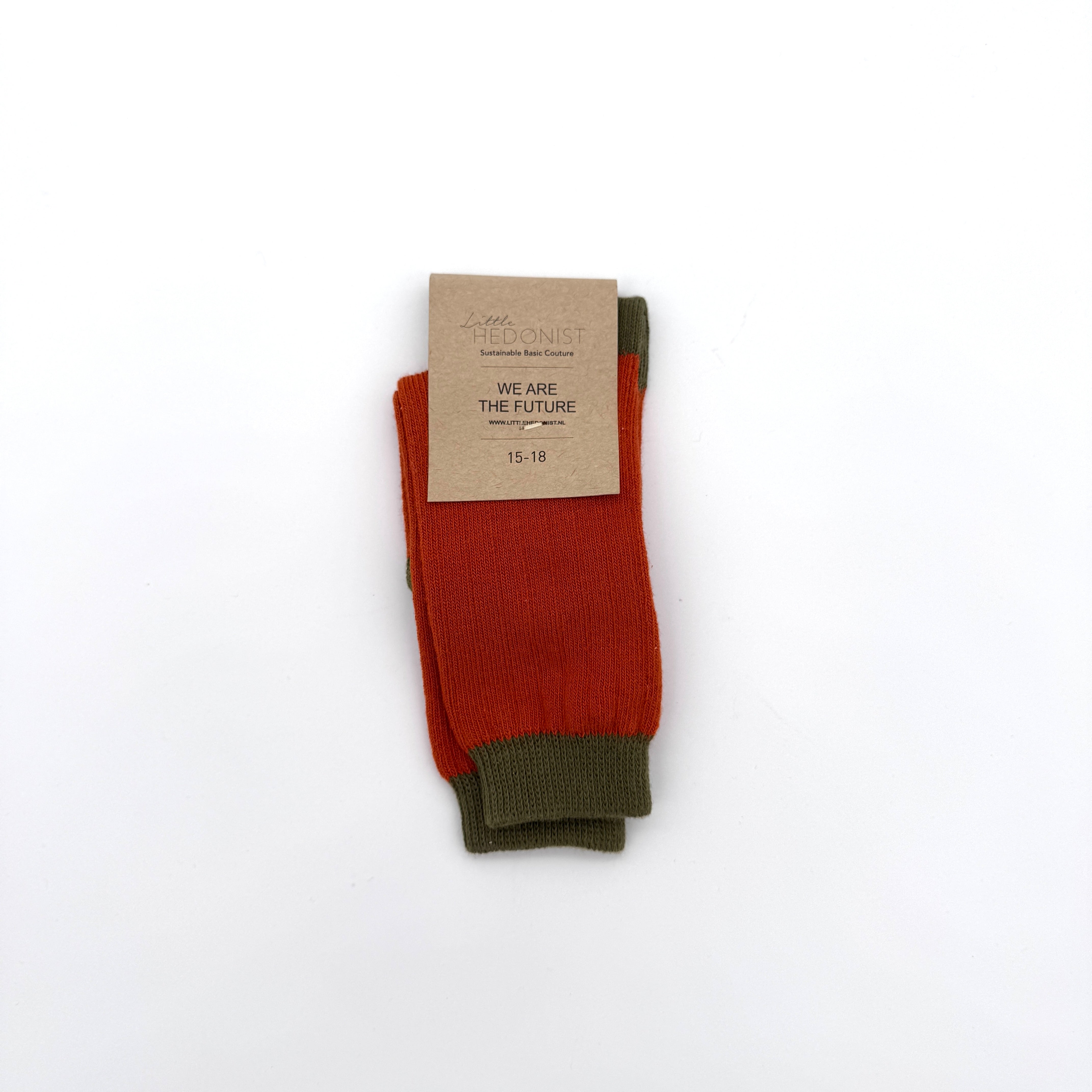 Ein Paar rote und olivgrüne Socken mit einem braunen Papieretikett mit der Aufschrift LITTLE HEDONIST, We Are The Future und der Größe 15-18, auf einem schlichten weißen Hintergrund.