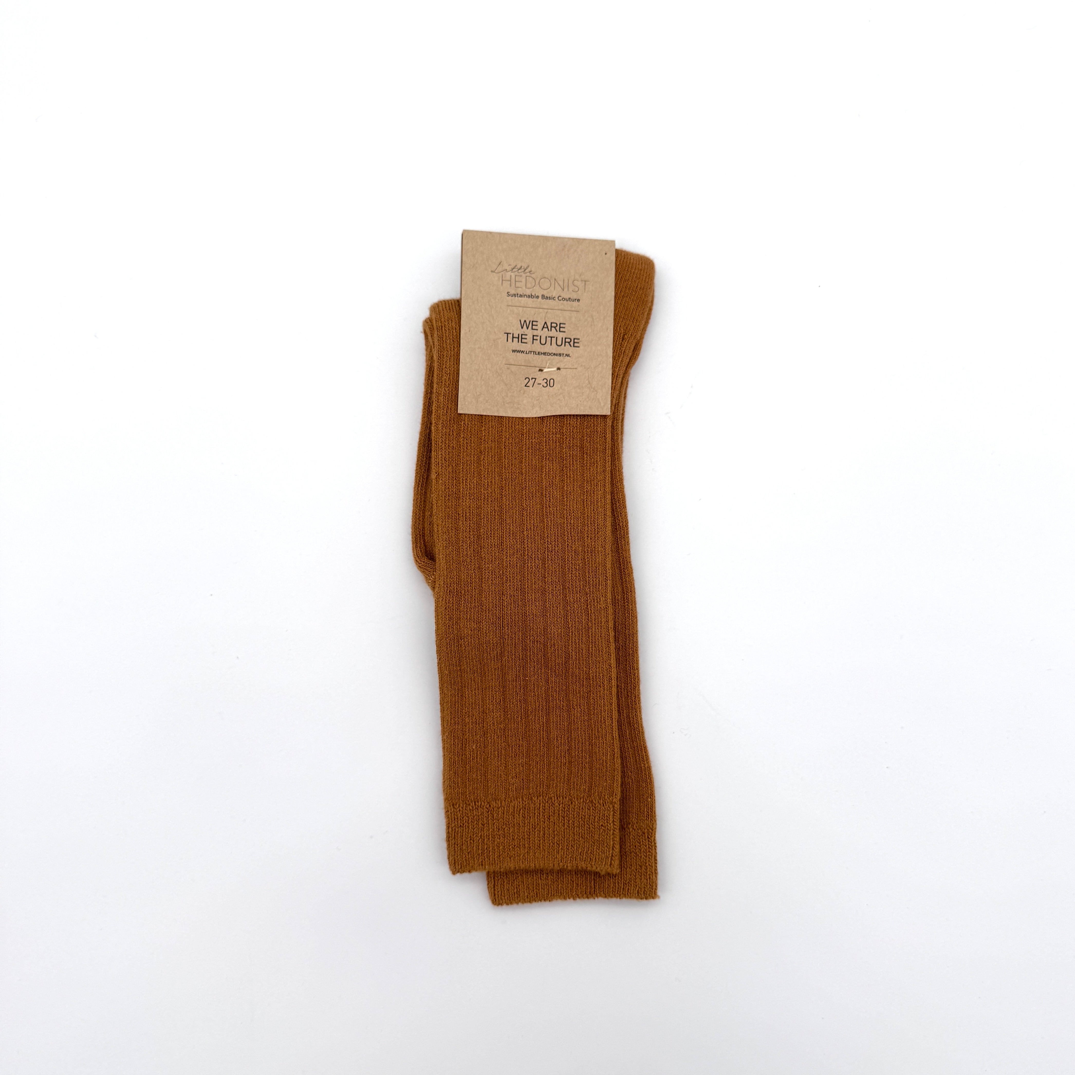 Ein Paar gefaltete, gerippte braune Socken mit einem Etikett aus Pappe mit der Aufschrift THE HEDONIST WE ARE THE FUTURE 27-30, das auf einem schlichten weißen Hintergrund angebracht ist.