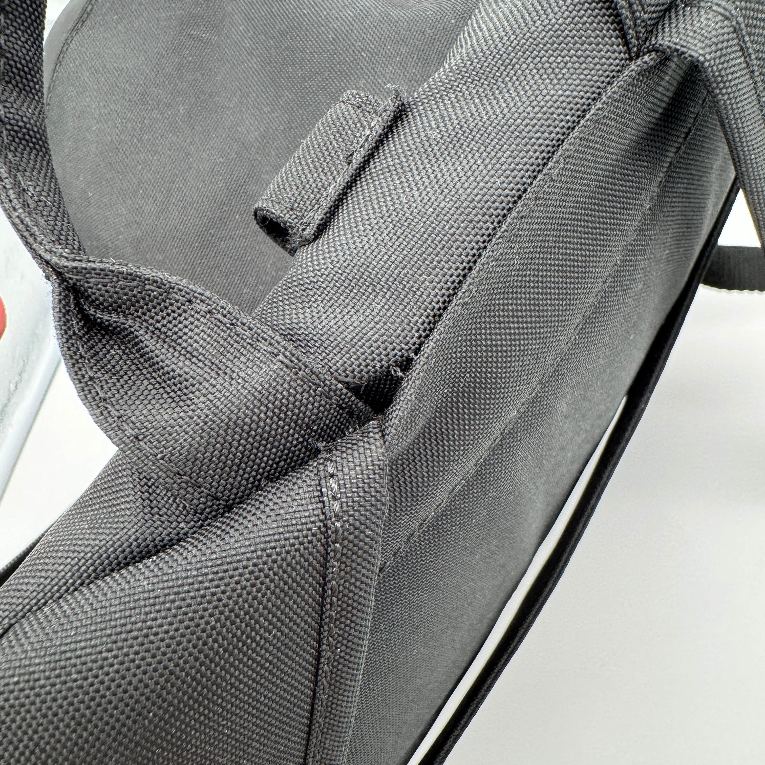 Nahaufnahme eines schwarzen Stoffrucksacks, die das strukturierte Material, einen Riemen und Nähte vor einem weißen Hintergrund zeigt.