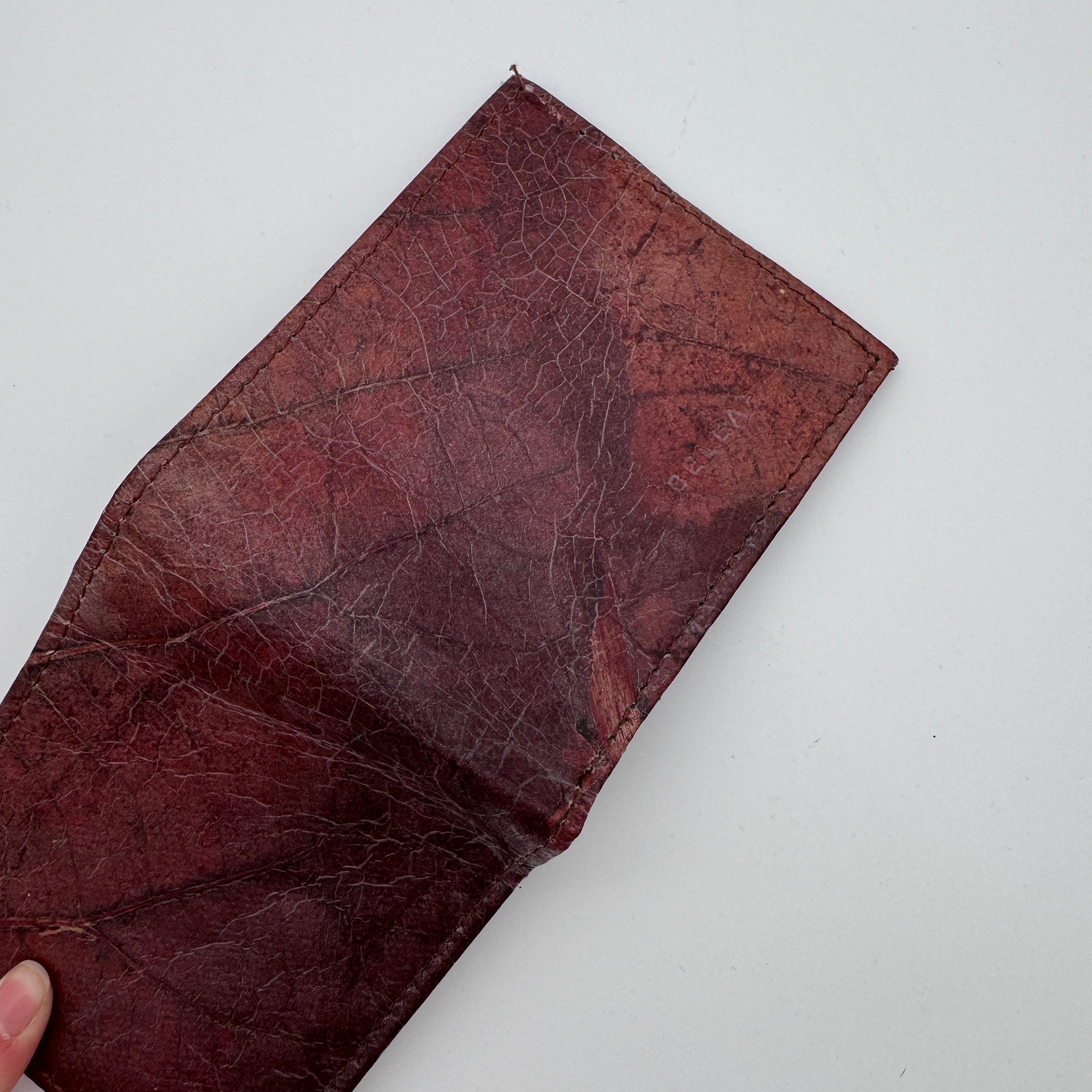 Eine Hand hält eine offene Brieftasche aus strukturiertem, kastanienbraunem Material mit sichtbaren Falten und Mustern. Das Portemonnaie ist leer und wird vor einem schlichten weißen Hintergrund gezeigt.