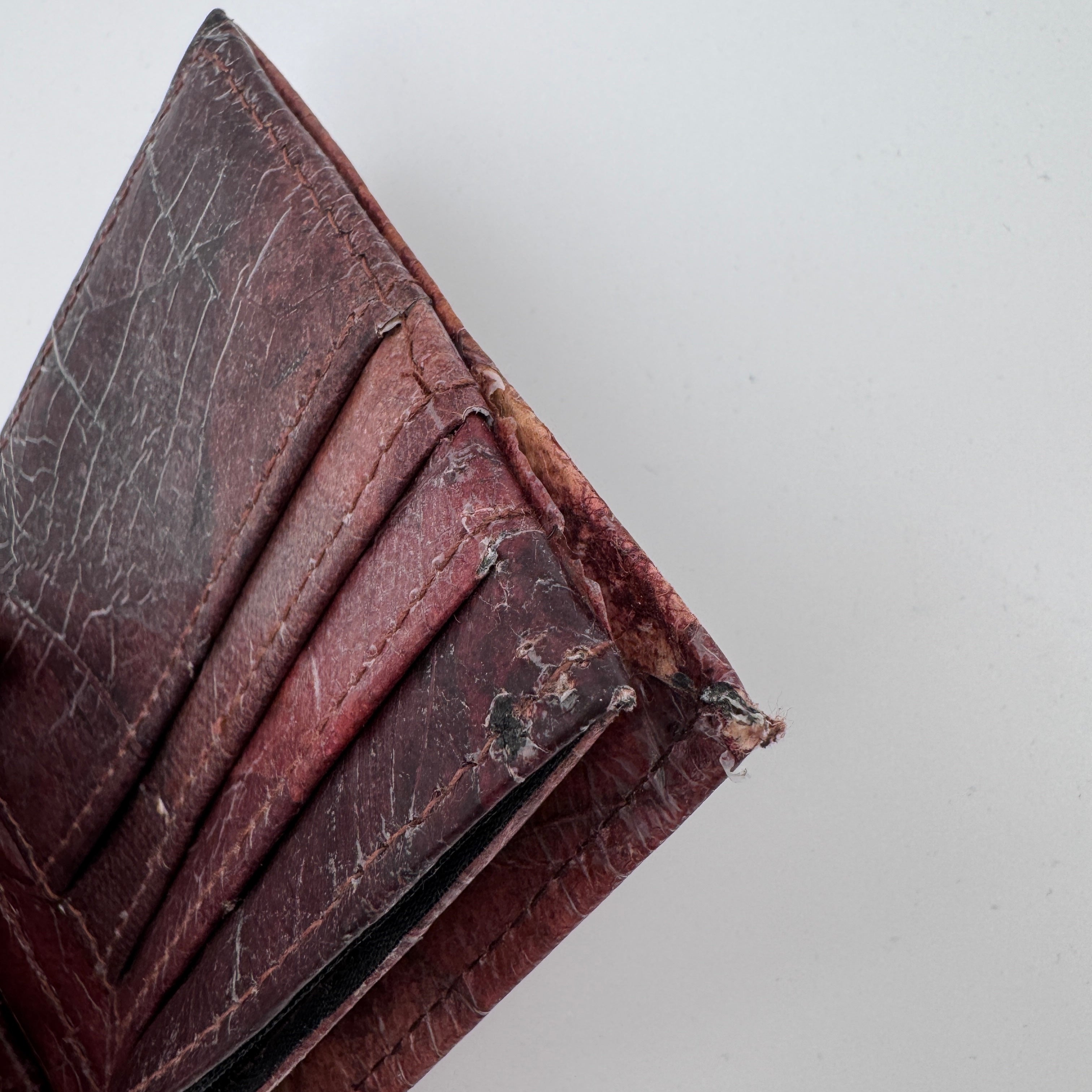 Nahaufnahme einer abgenutzten und beschädigten braunen Ledergeldbörse mit sichtbaren Rissen, Kratzern und ausgefransten Kanten vor einem schlichten weißen Hintergrund.