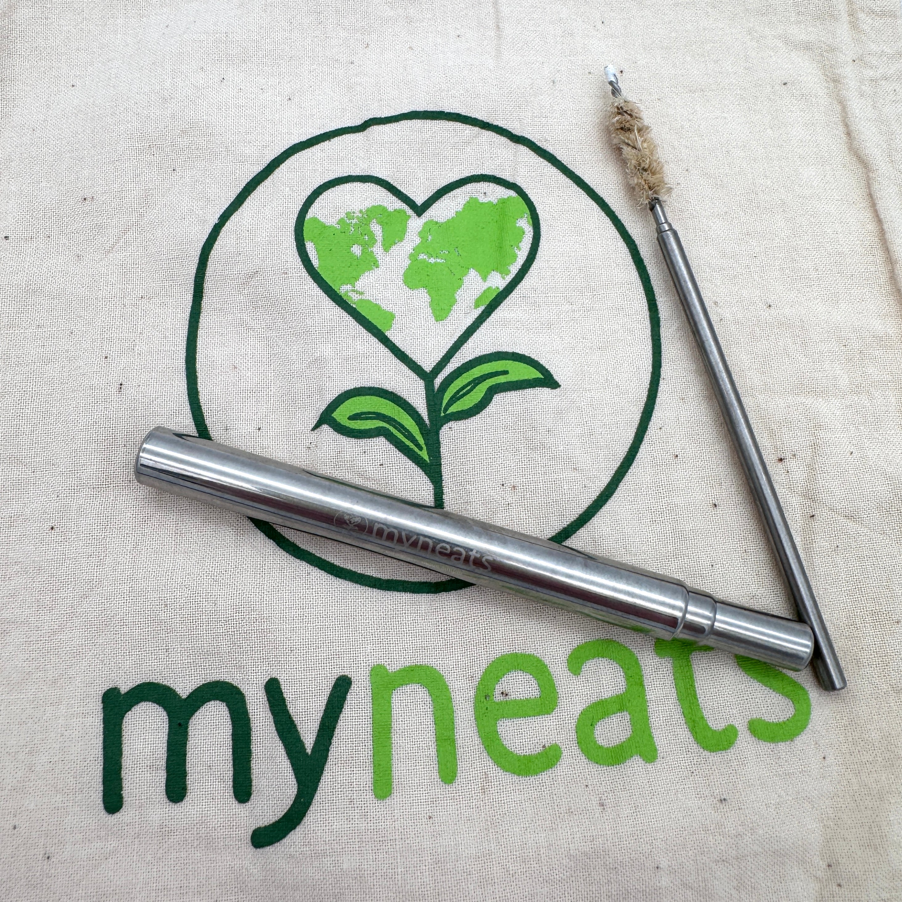 Ein wiederverwendbarer Metallstrohhalm und eine Reinigungsbürste befinden sich in einer Stofftasche mit einem grünen herzförmigen Earth and sprout-Logo über dem Text myneats.