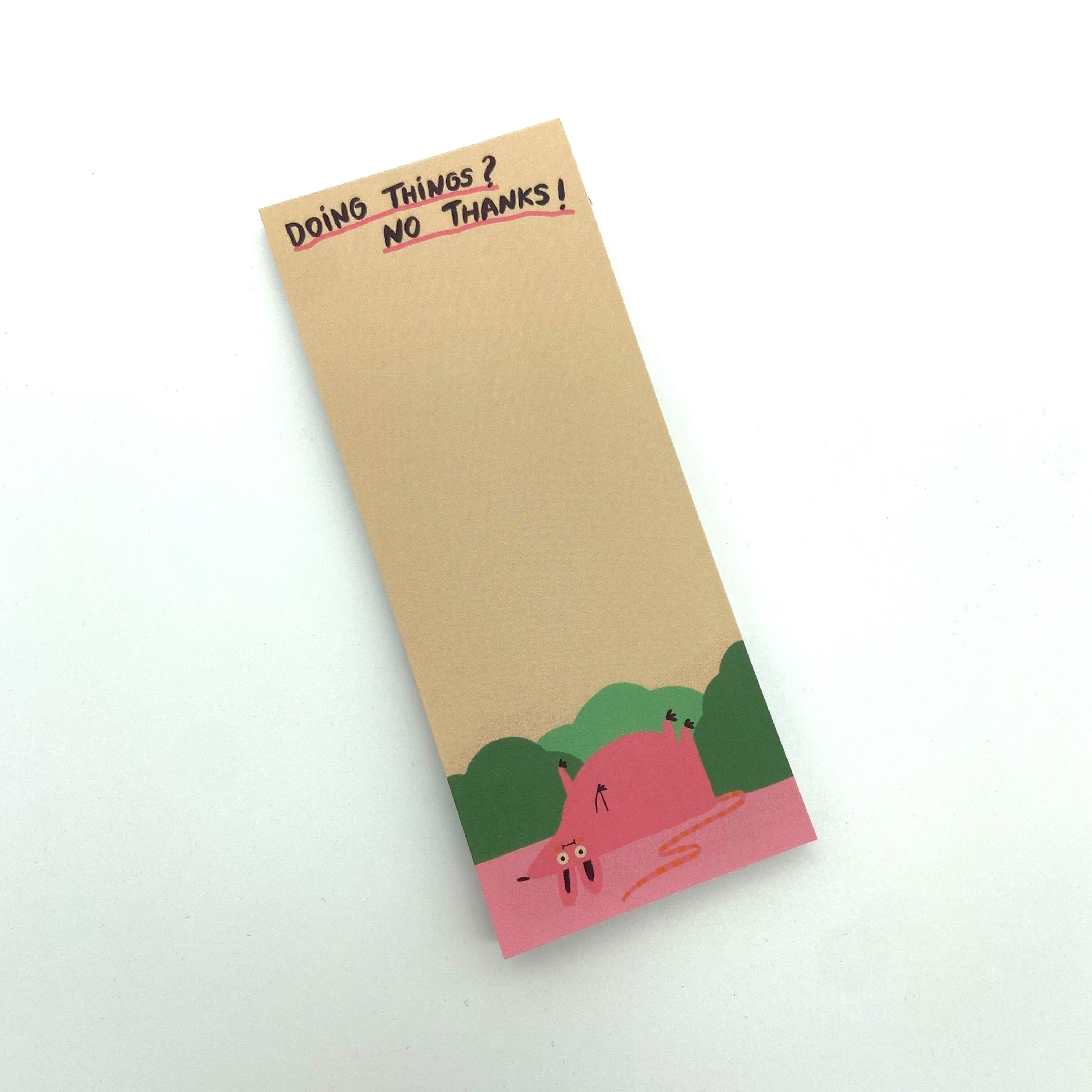 Notizblock mit der Aufschrift "Doing Things? No Thanks!" und einer pinken Figur, die in grünem Gebüsch liegt.