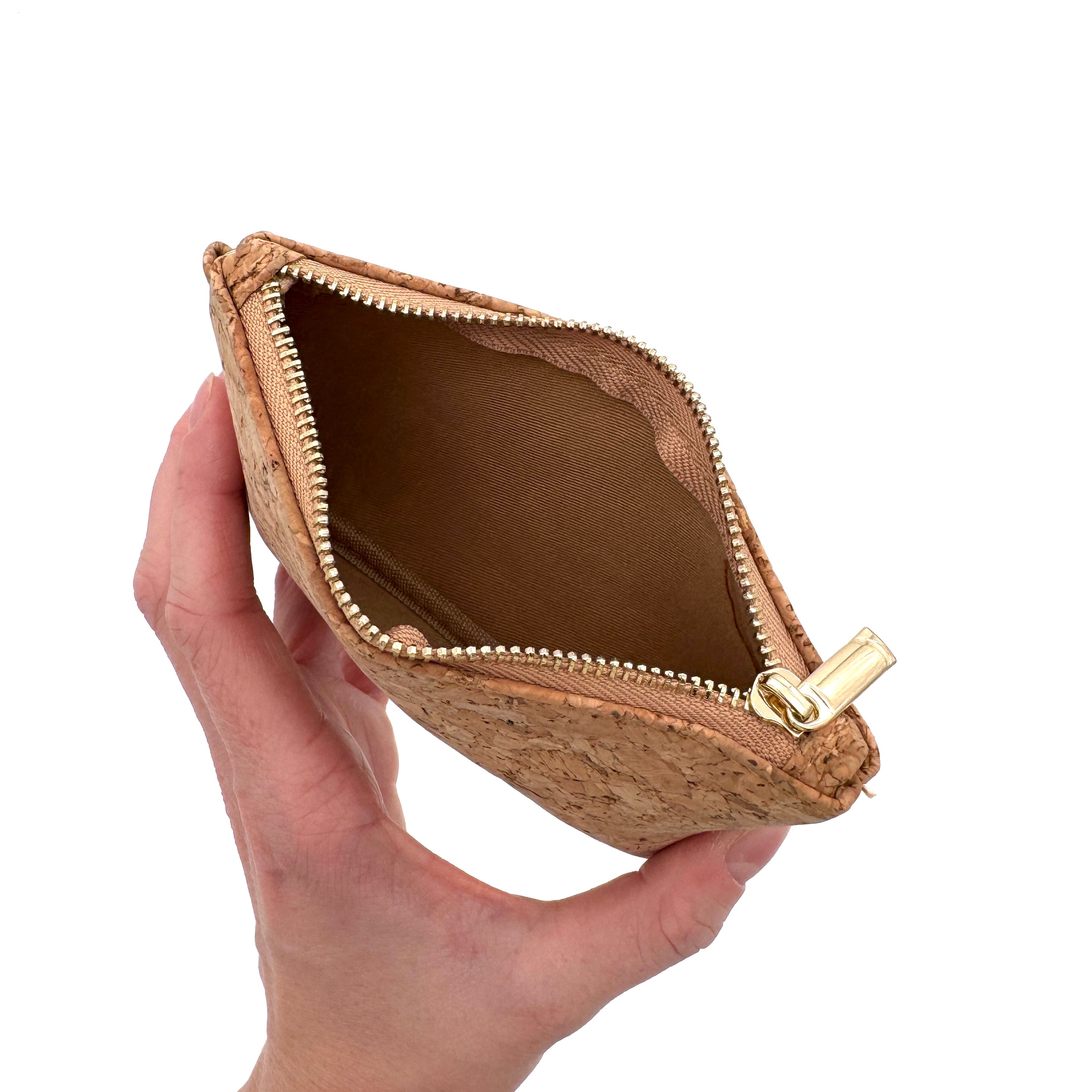 Eine Hand hält ein kleines, offenes Portemonnaie aus Kork mit einem goldenen Reißverschluss, dessen leeres Inneres aus braunem Stoff vor einem weißen Hintergrund zu sehen ist.